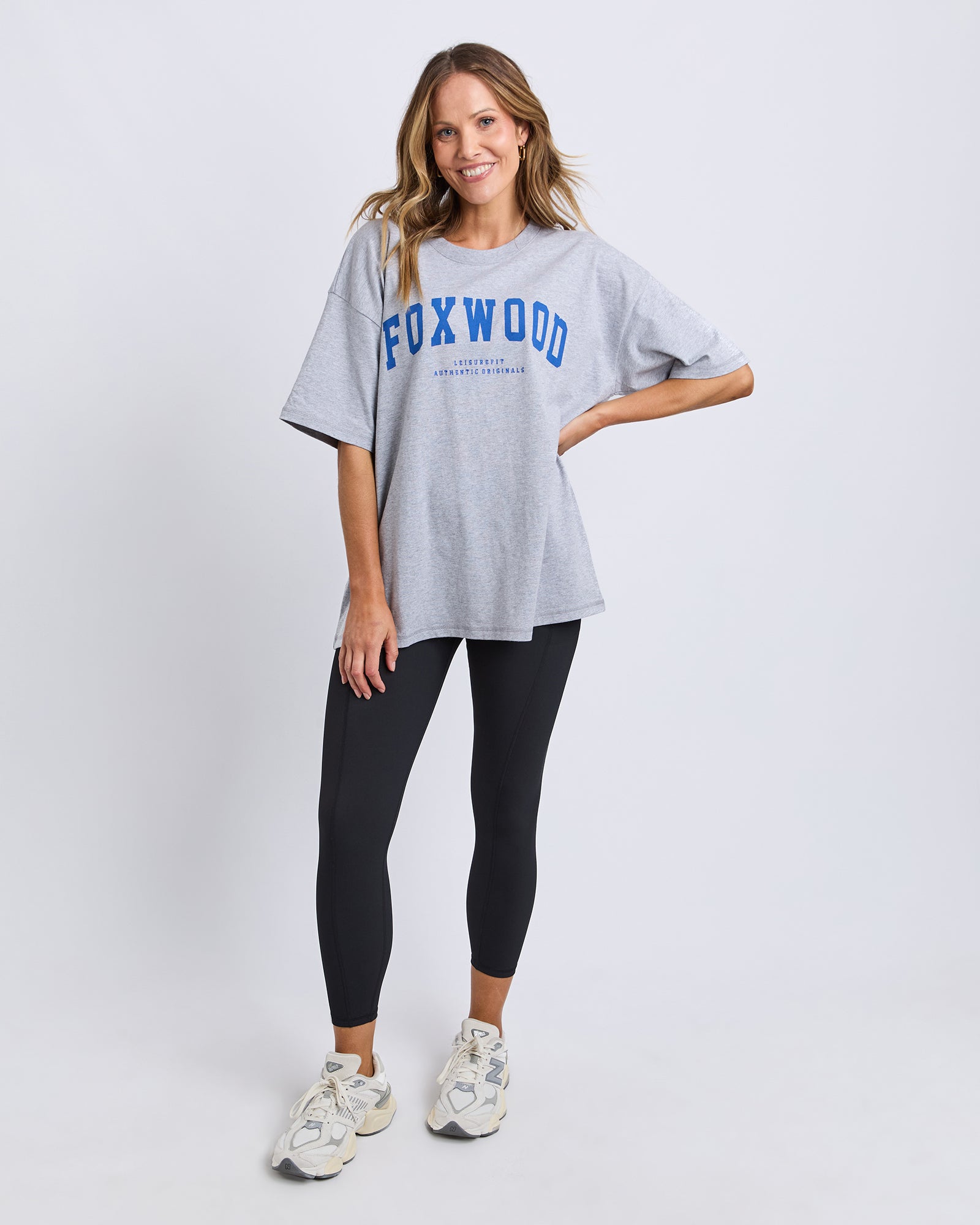 Woman wearing a grey 'FOXWOOD' t-shirt  with blue print and black leggings on a white background
