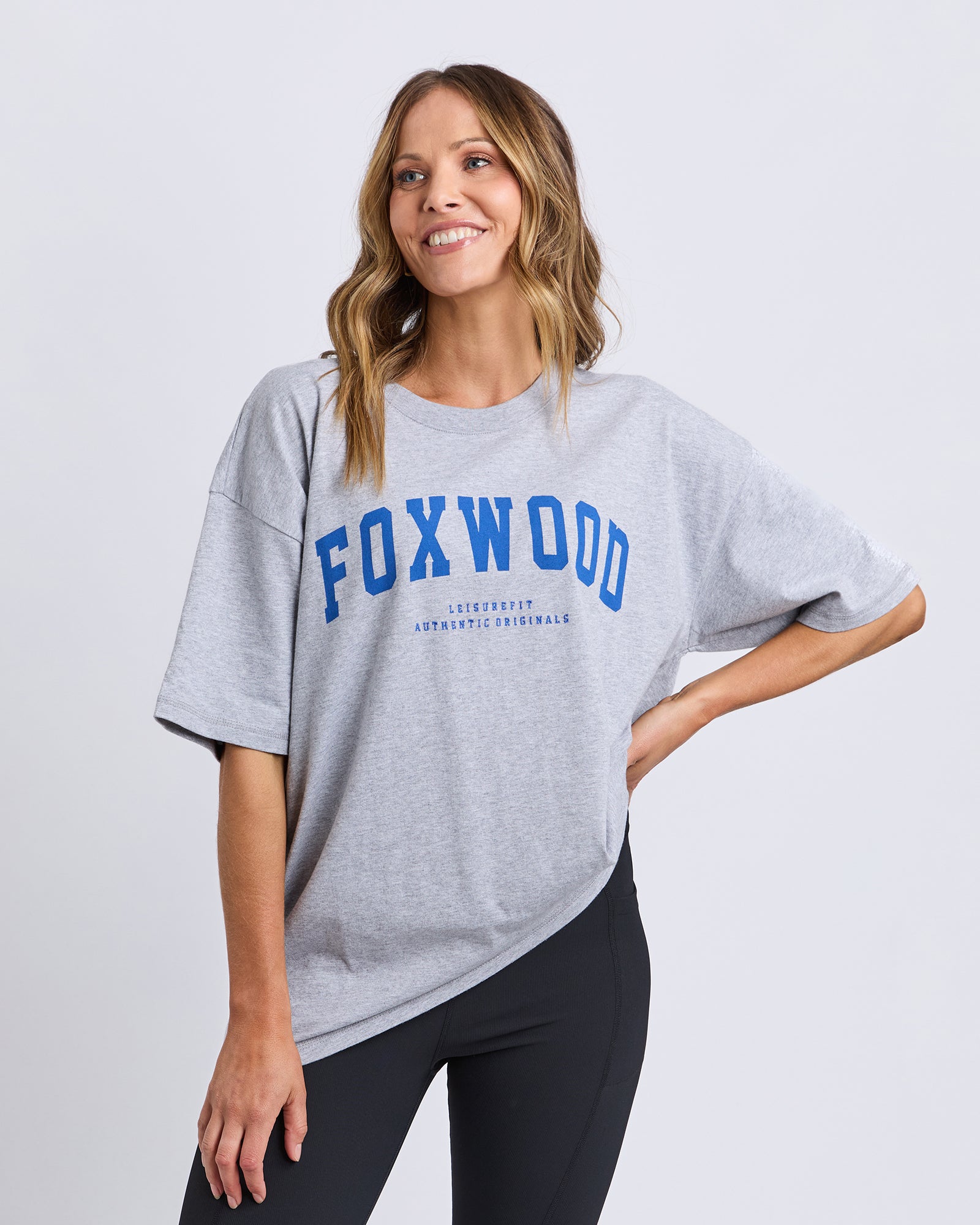 Woman wearing a Foxwood grey t-shirt with 'FOXWOOD' printed on it in blue against a white background