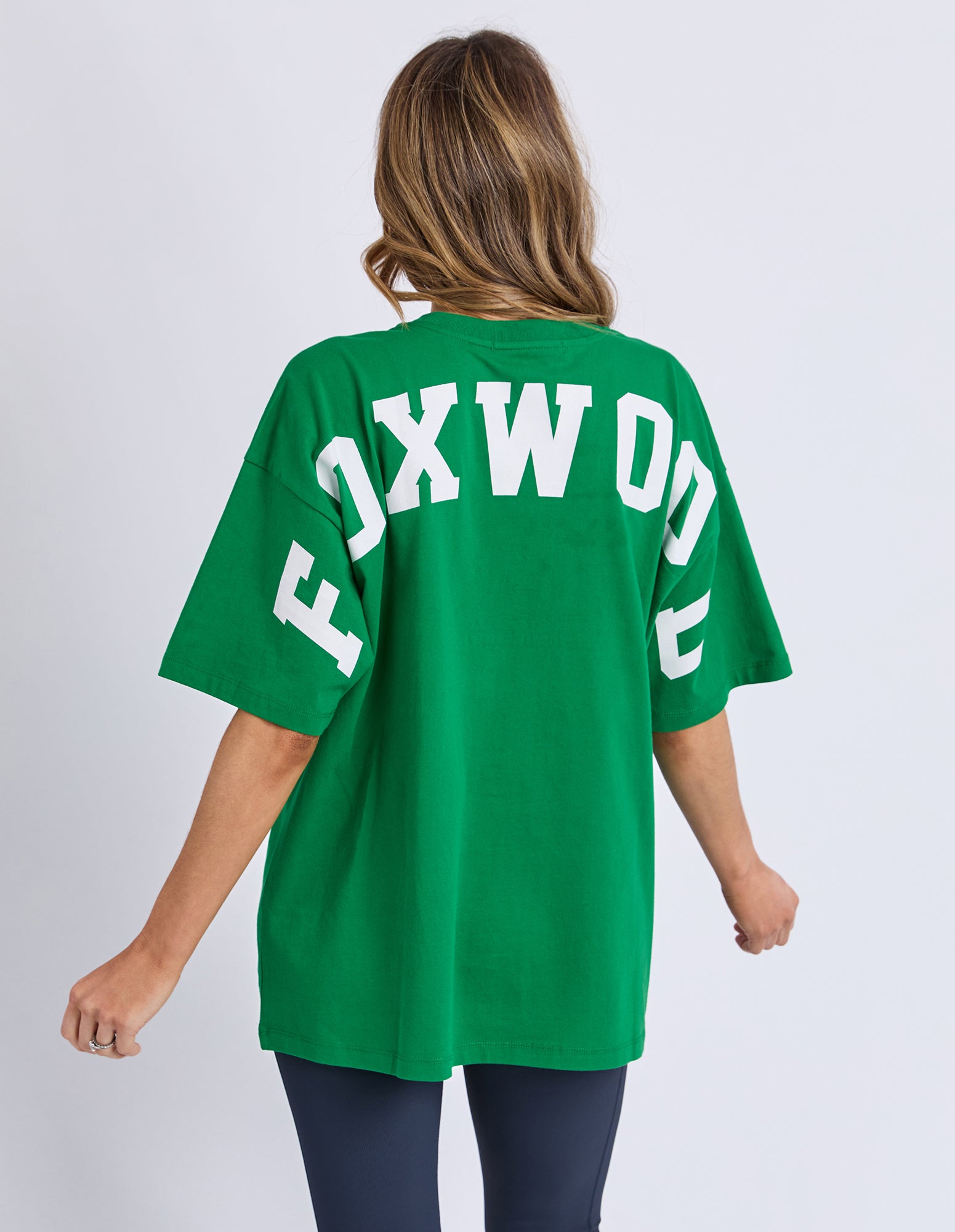 Woman wearing a Foxwood green oversized t-shirt with 'FOXWOOD' printed on the back against a white background