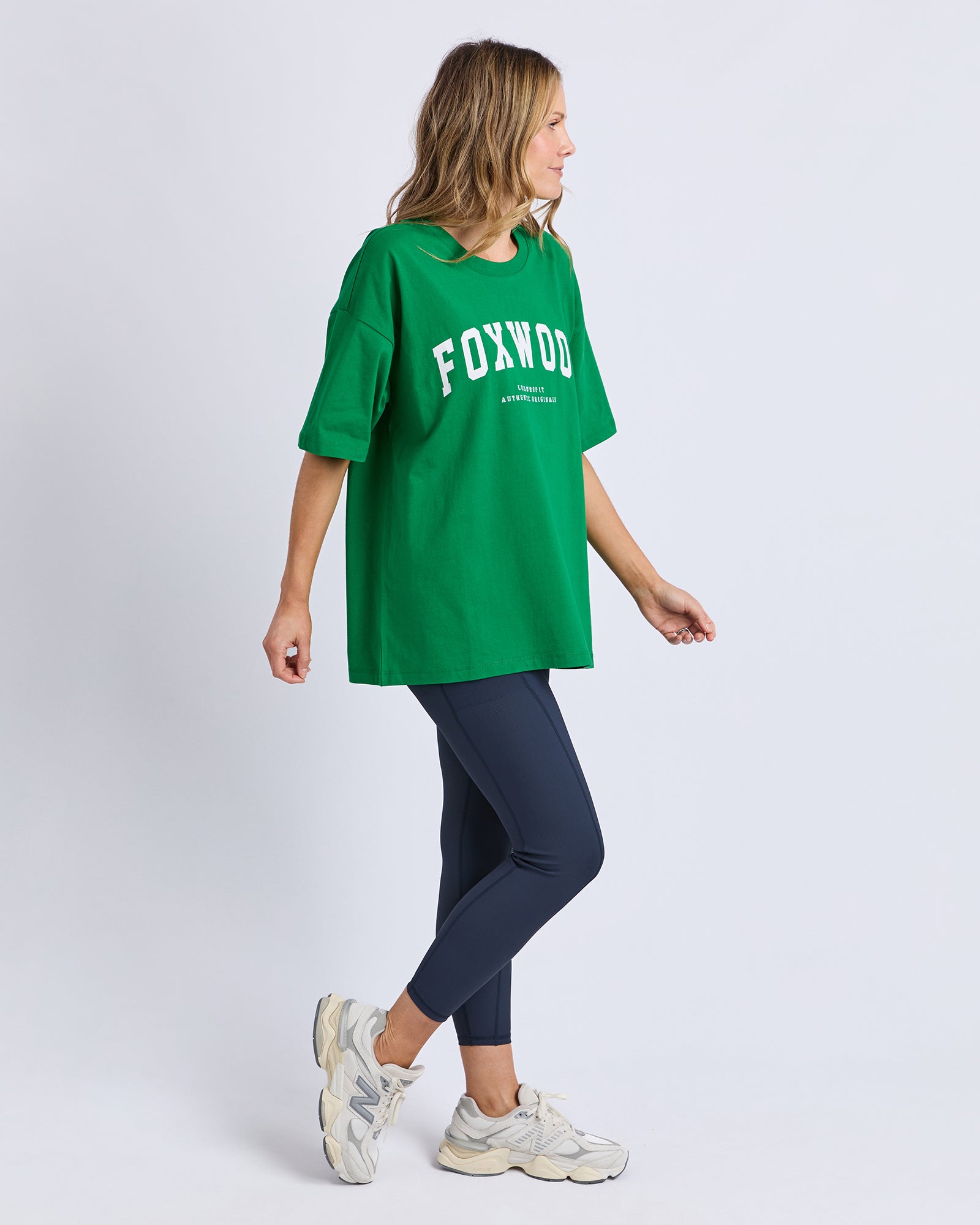 Woman wearing a green 'FOXWOOD' t-shirt and dark pants on a white background