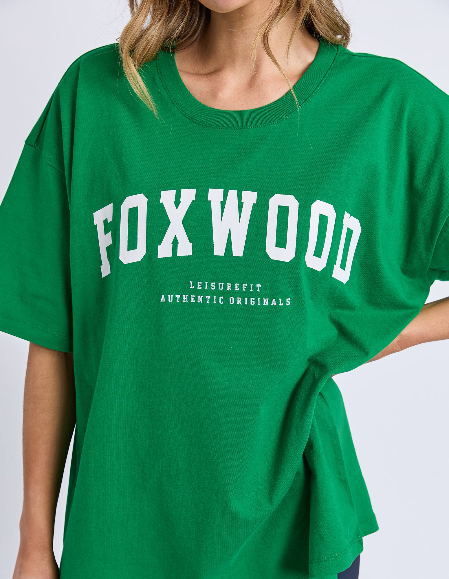 Green t-shirt with 'FOXWOOD' printed on it in white text against a white background