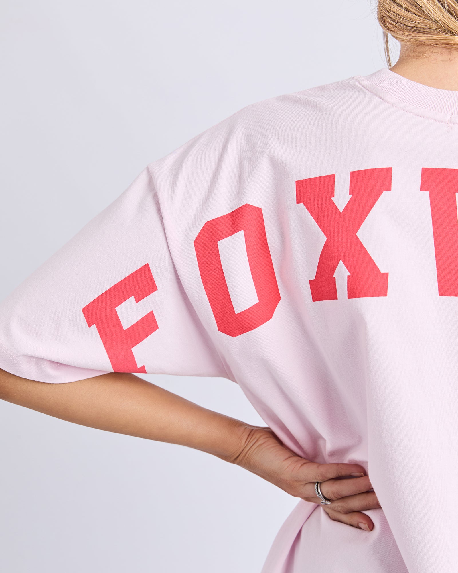 Collection of Woman wearing a Foxwood light pink t-shirt with 'FOXWOOD' printed in red on a plain background in a gallery layout
