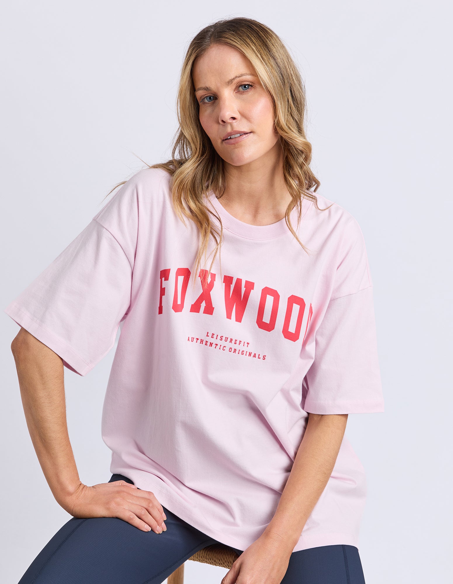 Woman wearing a pink t-shirt with 'FOXWOOD' printed on it against a light gray background