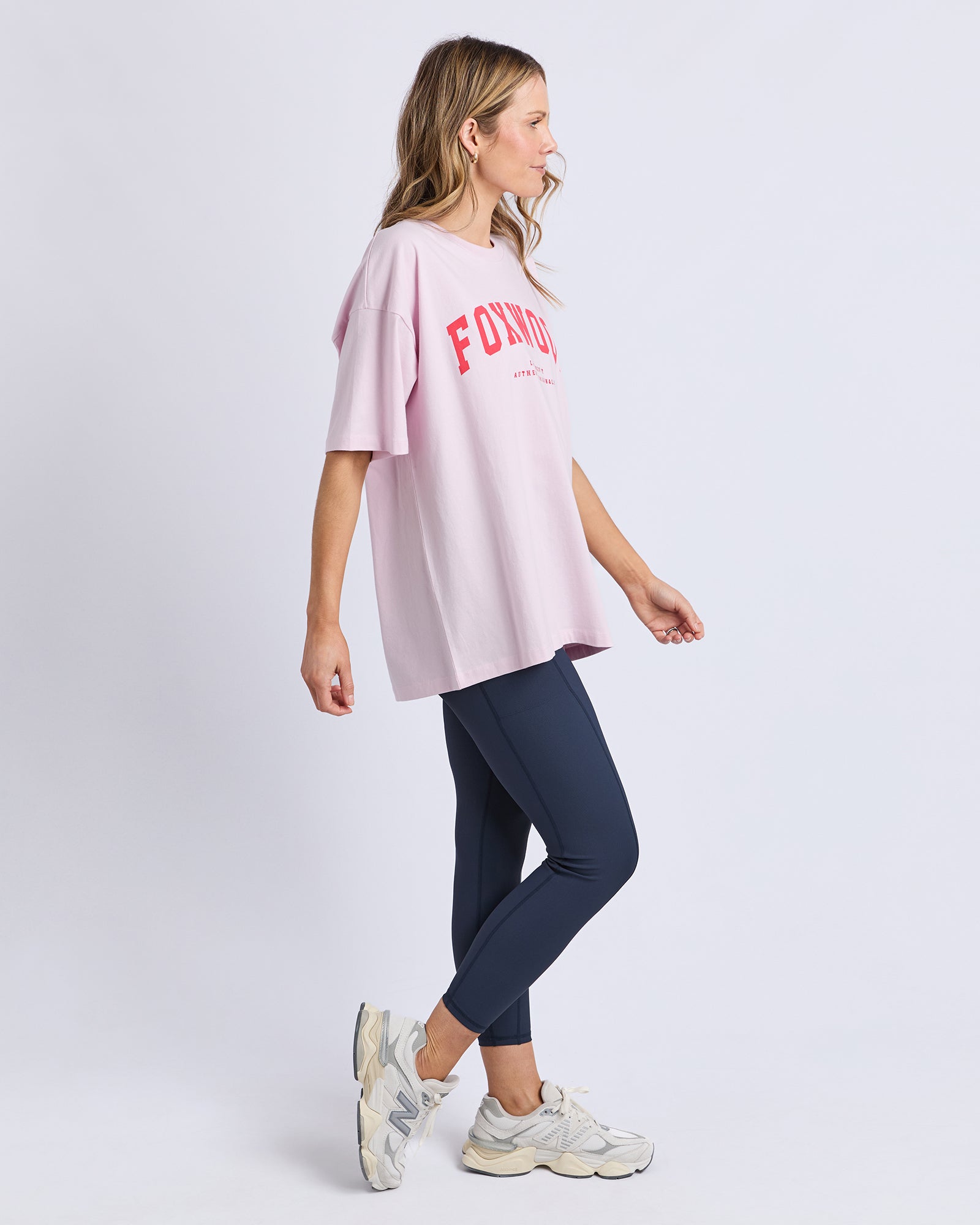 Woman wearing a light pink oversized t-shirt with 'FOXWOOD' logo and navy leggings on a white background