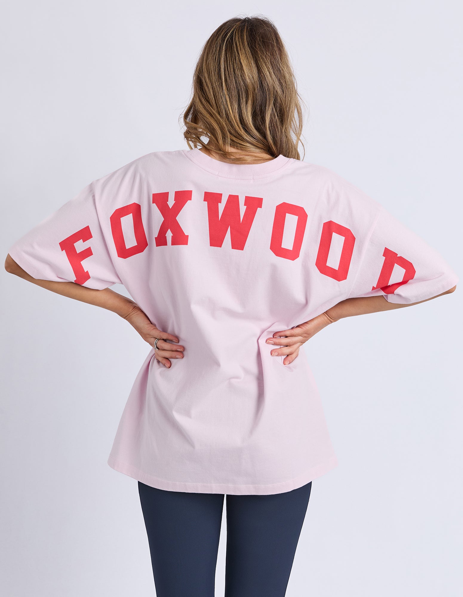 Collection of Woman wearing a pink t-shirt with 'FOXWOOD' printed on the back against a white background in a gallery layout