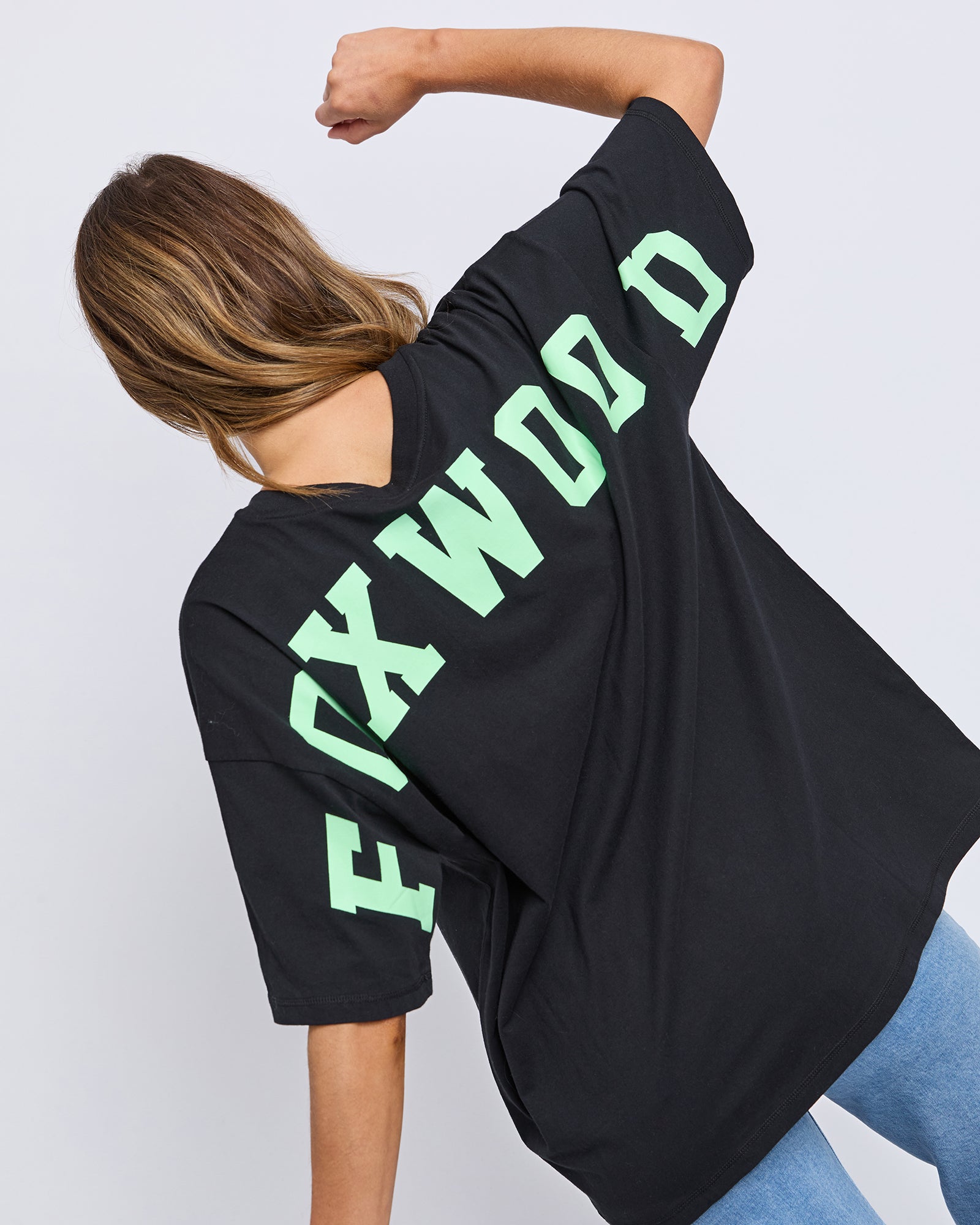Collection of Woman wearing a Foxwood black oversized t-shirt with green text on the back against a light grey background in a gallery layout