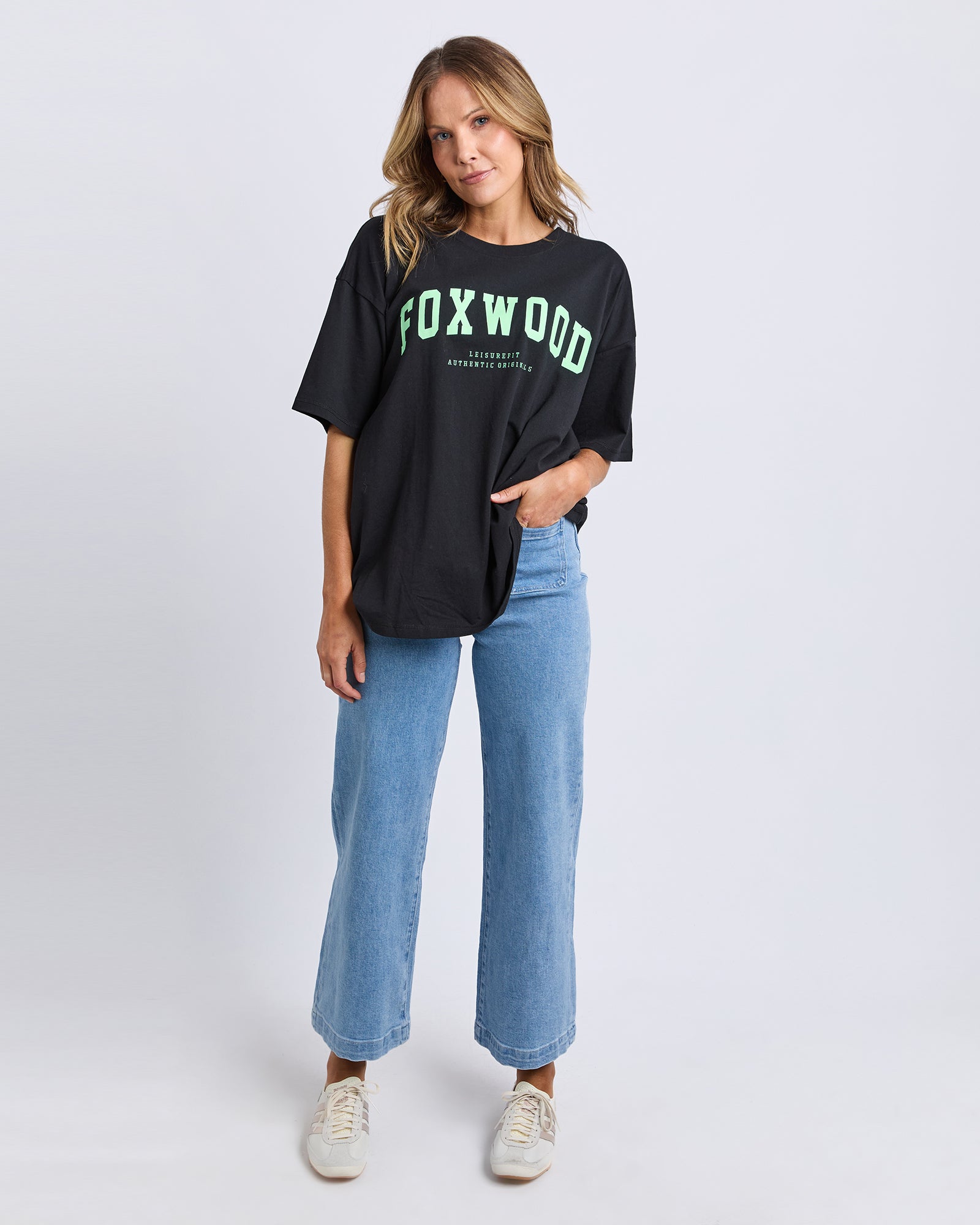 Collection of Woman wearing a Foxwood black t-shirt with 'FOXWOOD' printed on it in green, standing against a white background in a gallery layout