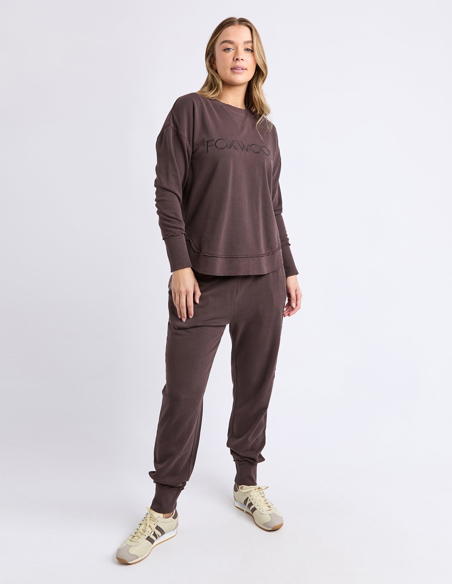 Woman wearing a brown tracksuit with a visible Foxwood brand logo on a white background