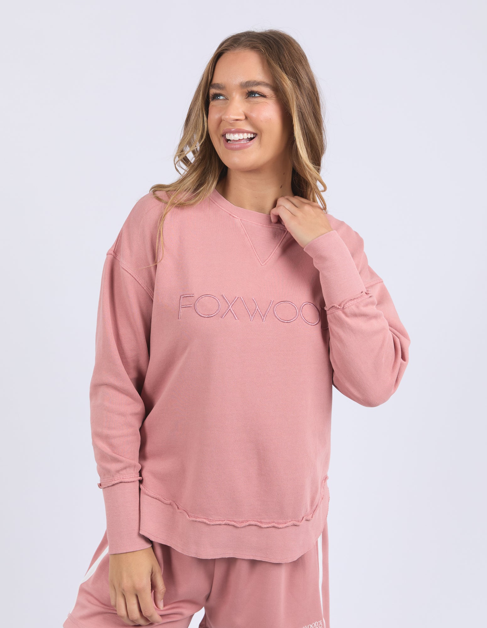 Woman wearing a dusty rose jumper with 'FOXWOOD' branding on a light grey background