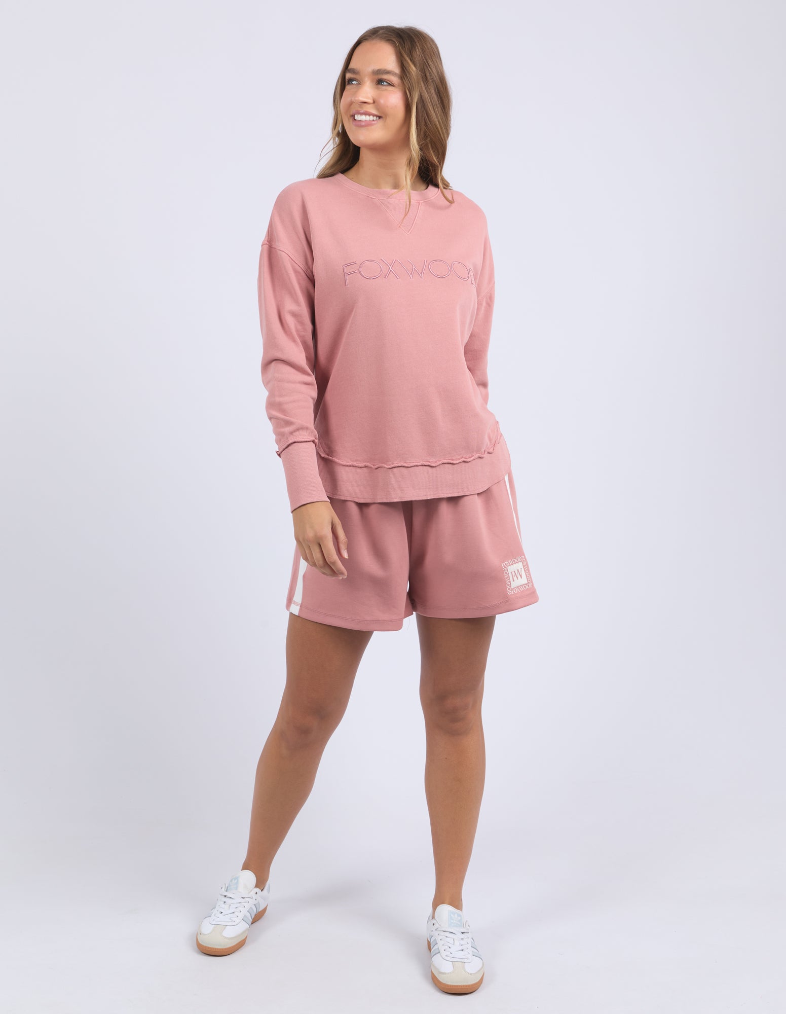 Woman wearing a dusty rose jumper with Foxwood on the chest and shorts on a white background