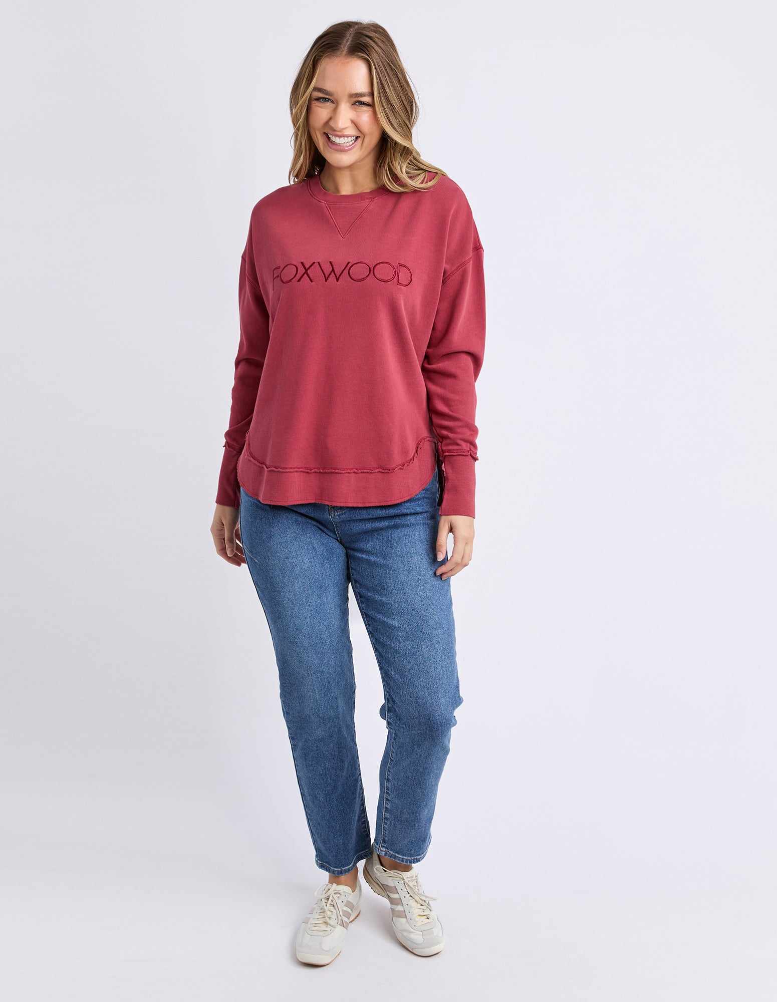 Image of Woman wearing a red 'Foxwood' jumper and blue jeans on a white background