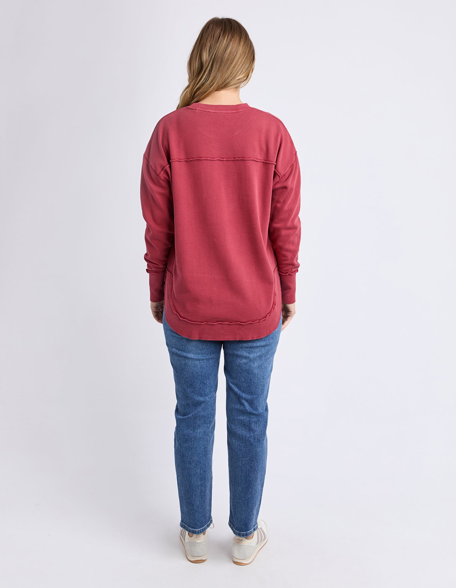 Woman wearing a red Foxwood jumper, back view and blue jeans on a white background