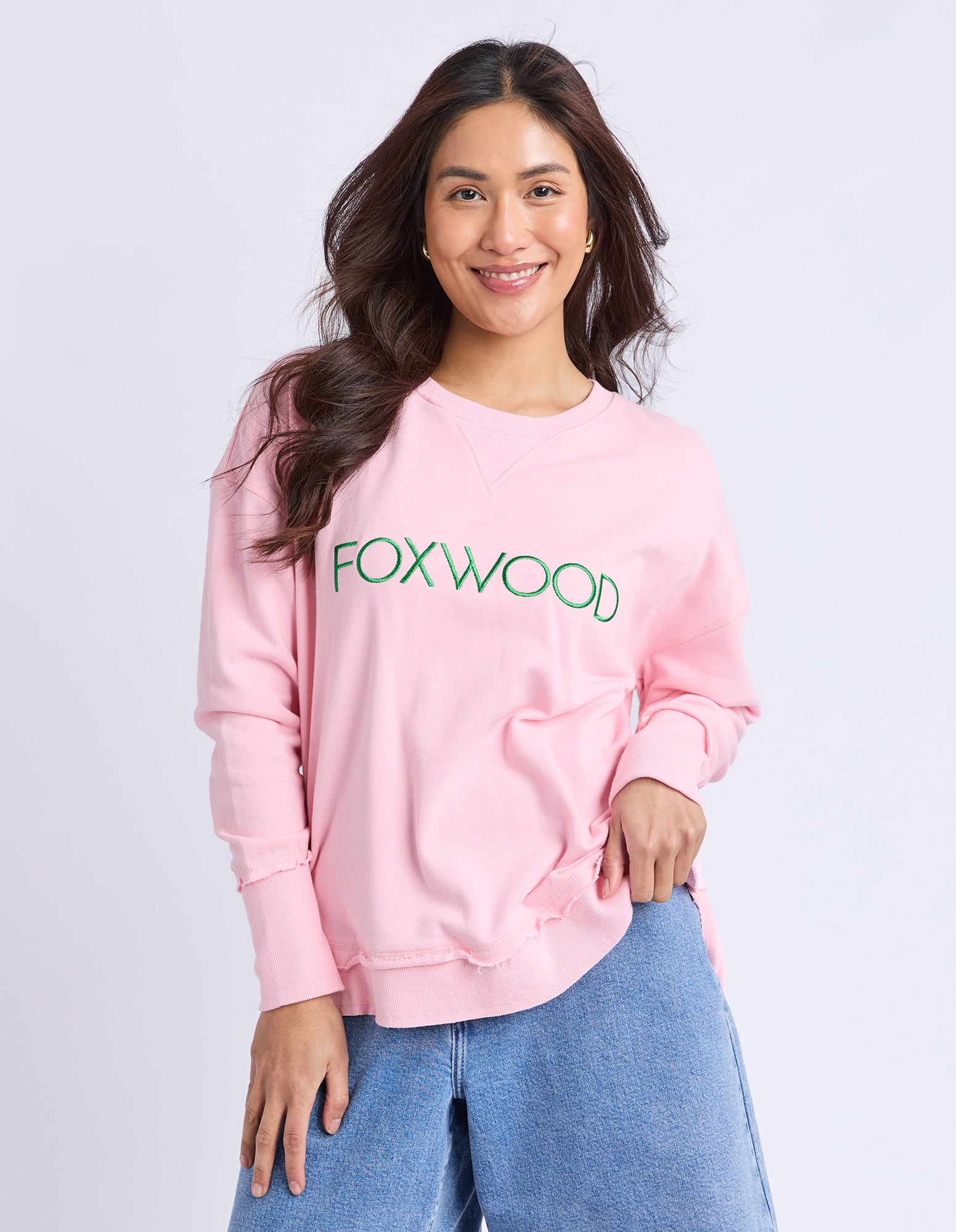 Collection of Woman wearing a pink jumper with 'FOXWOOD' text in emerald green on a plain background in a gallery layout