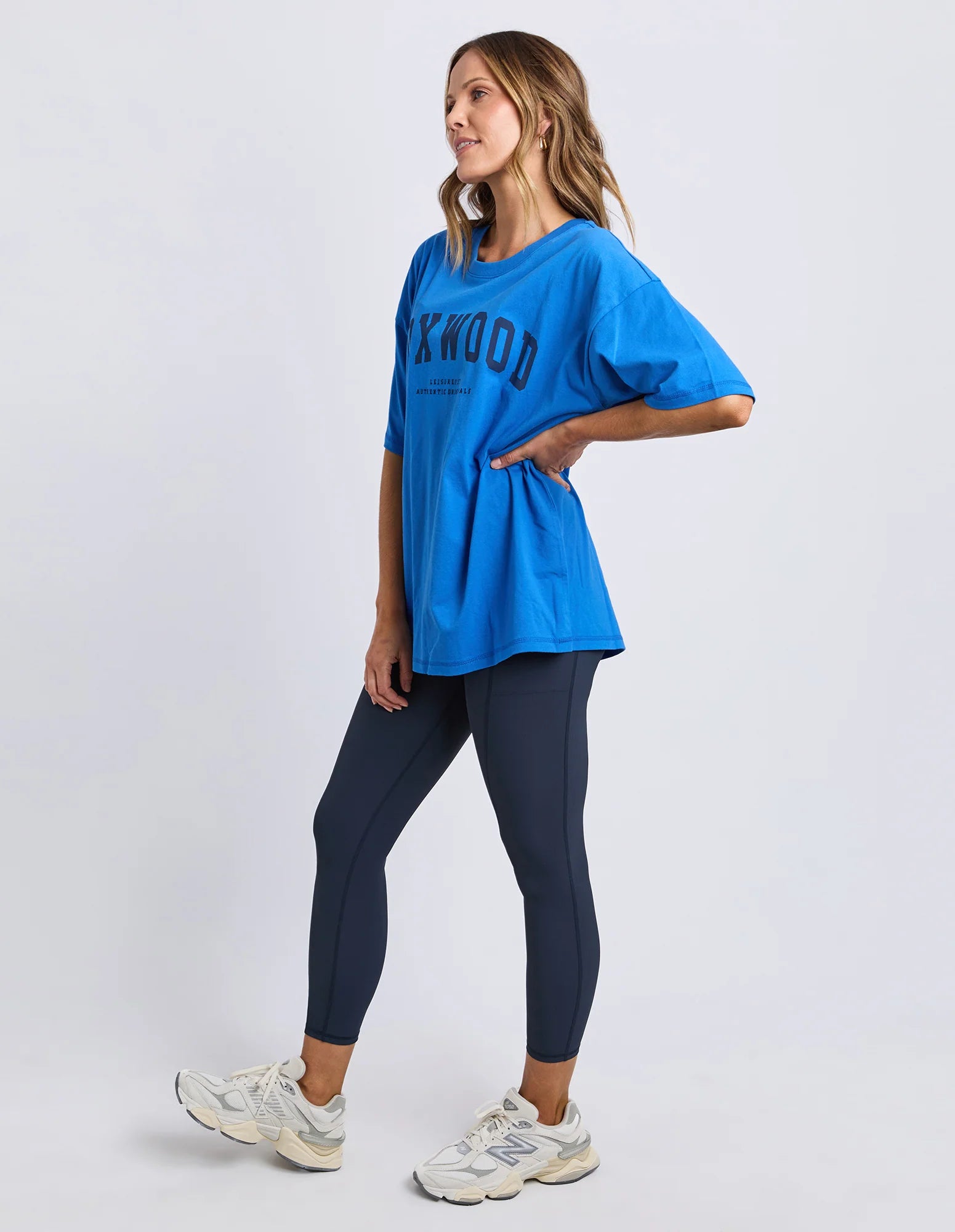 Image of Woman wearing a blue oversized Foxwood Interval t-shirt and dark leggings on a white background