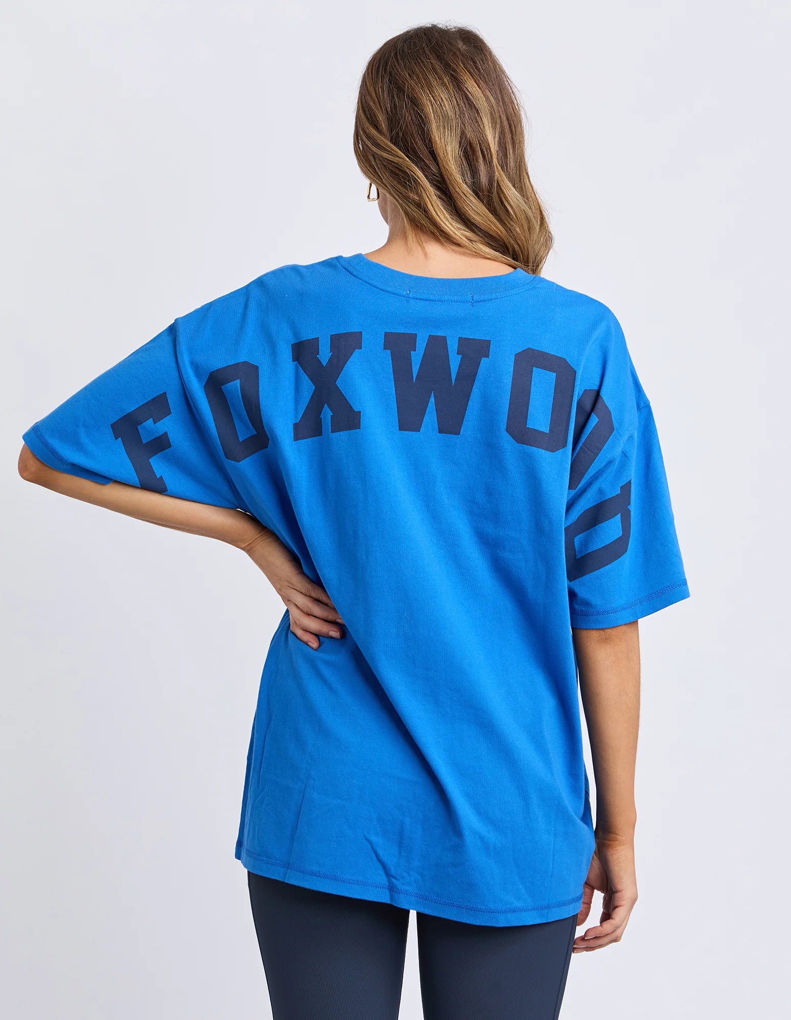 Image of Woman wearing a Foxwood blue t-shirt with 'FOXWOOD' branding on the back against a white background