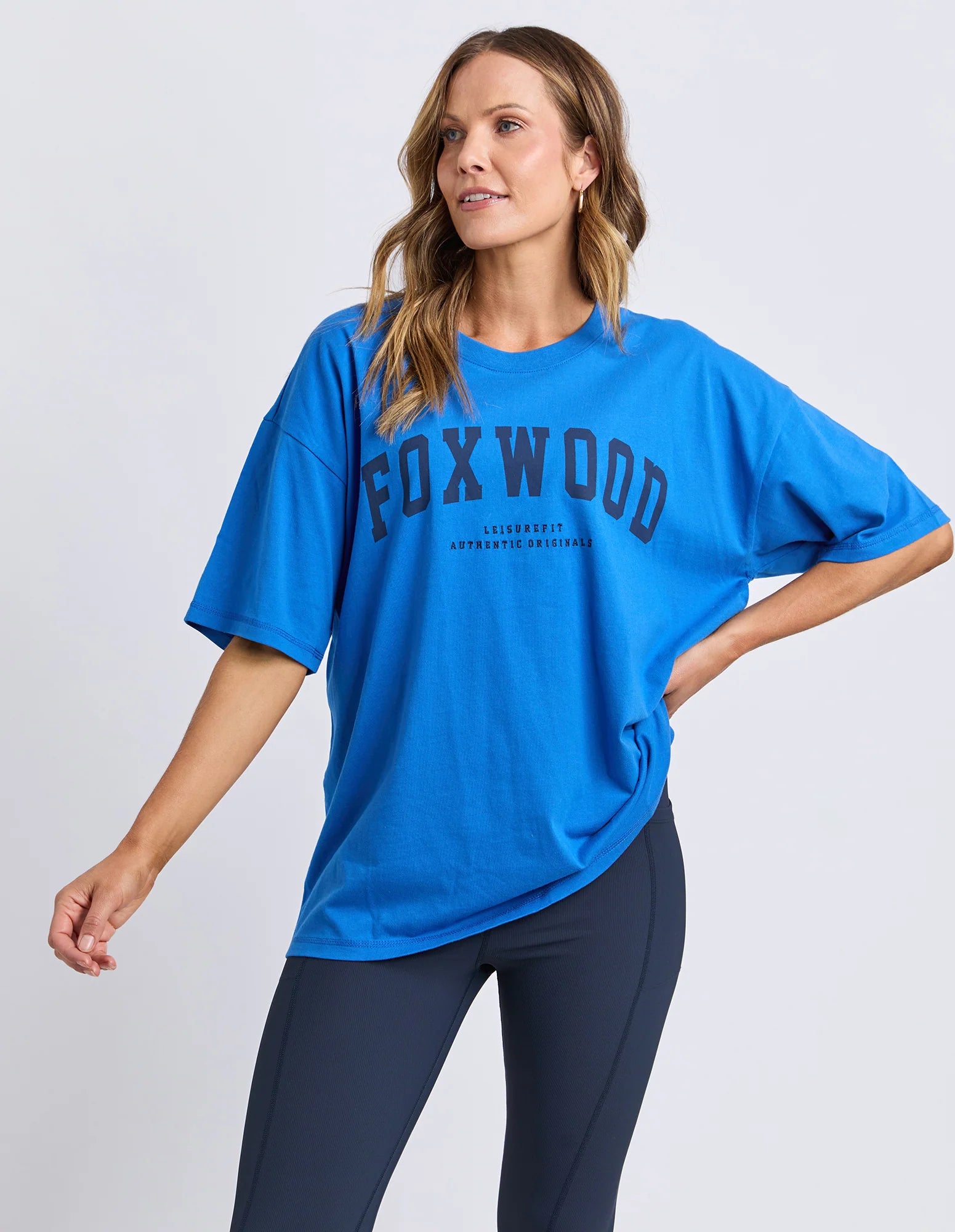 Image of Woman wearing a blue 'FOXWOOD' t-shirt  with navy branding on a light grey background