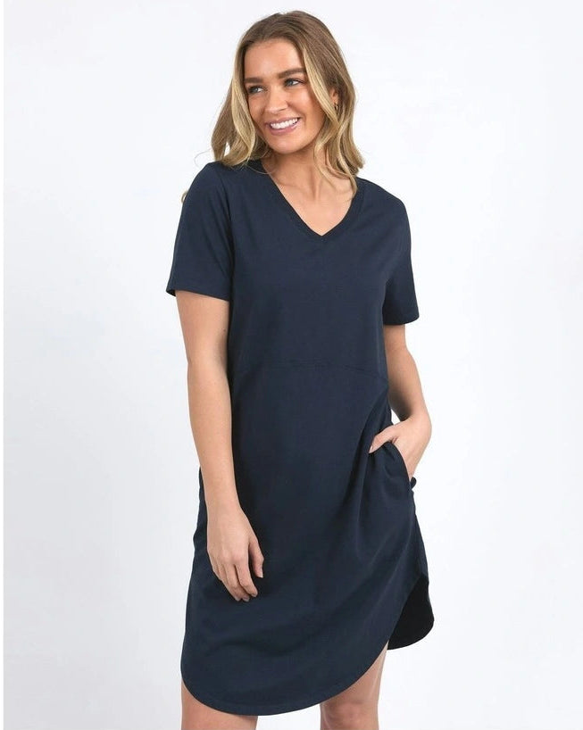 A woman modeling a Foxwood navy blue short-sleeve V-neck dress with side pockets, photographed against a plain white studio background.