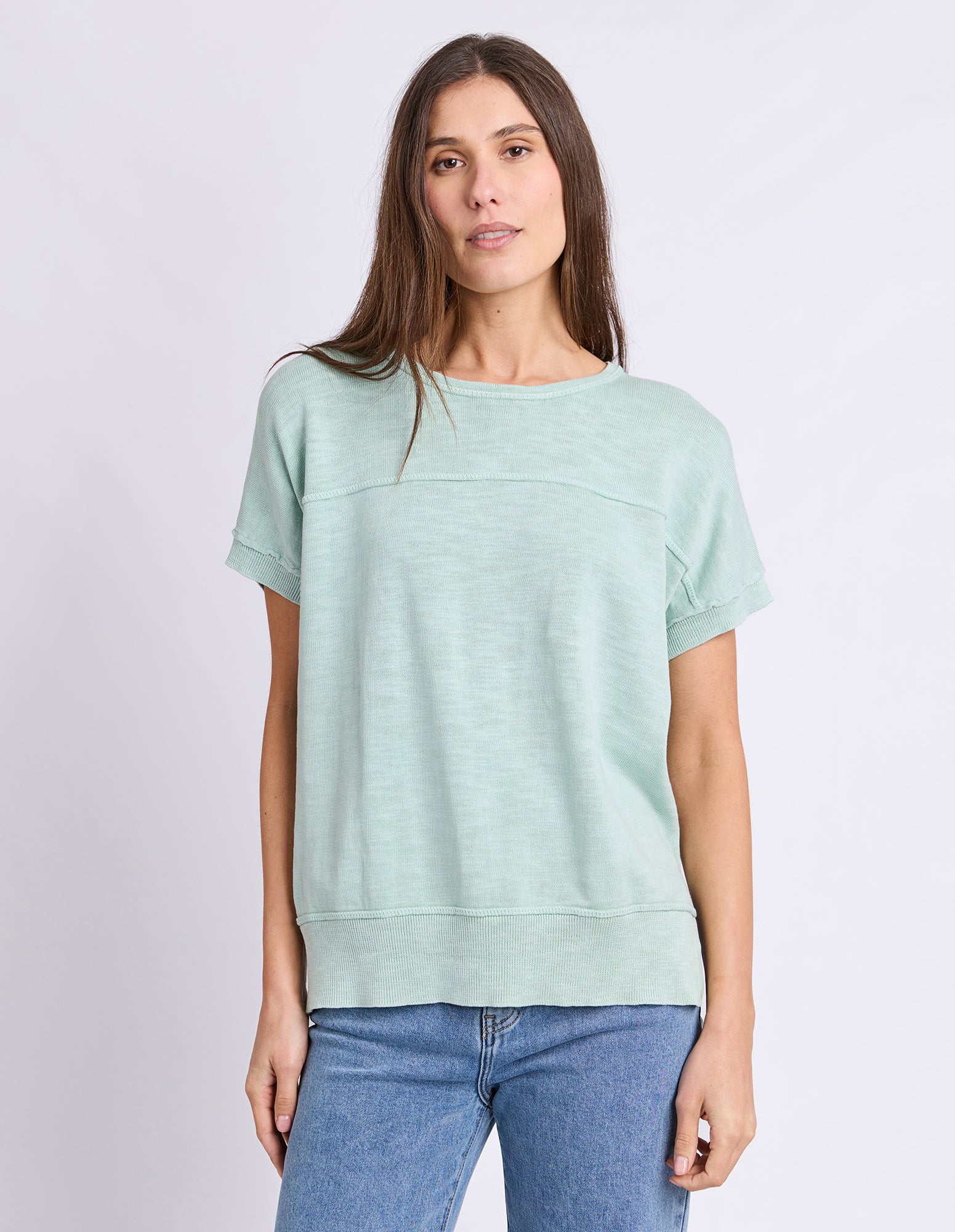 Image of A woman wearing a Foxwood light mint green short-sleeve crewneck sweatshirt and blue jeans, standing against a light gray studio background.