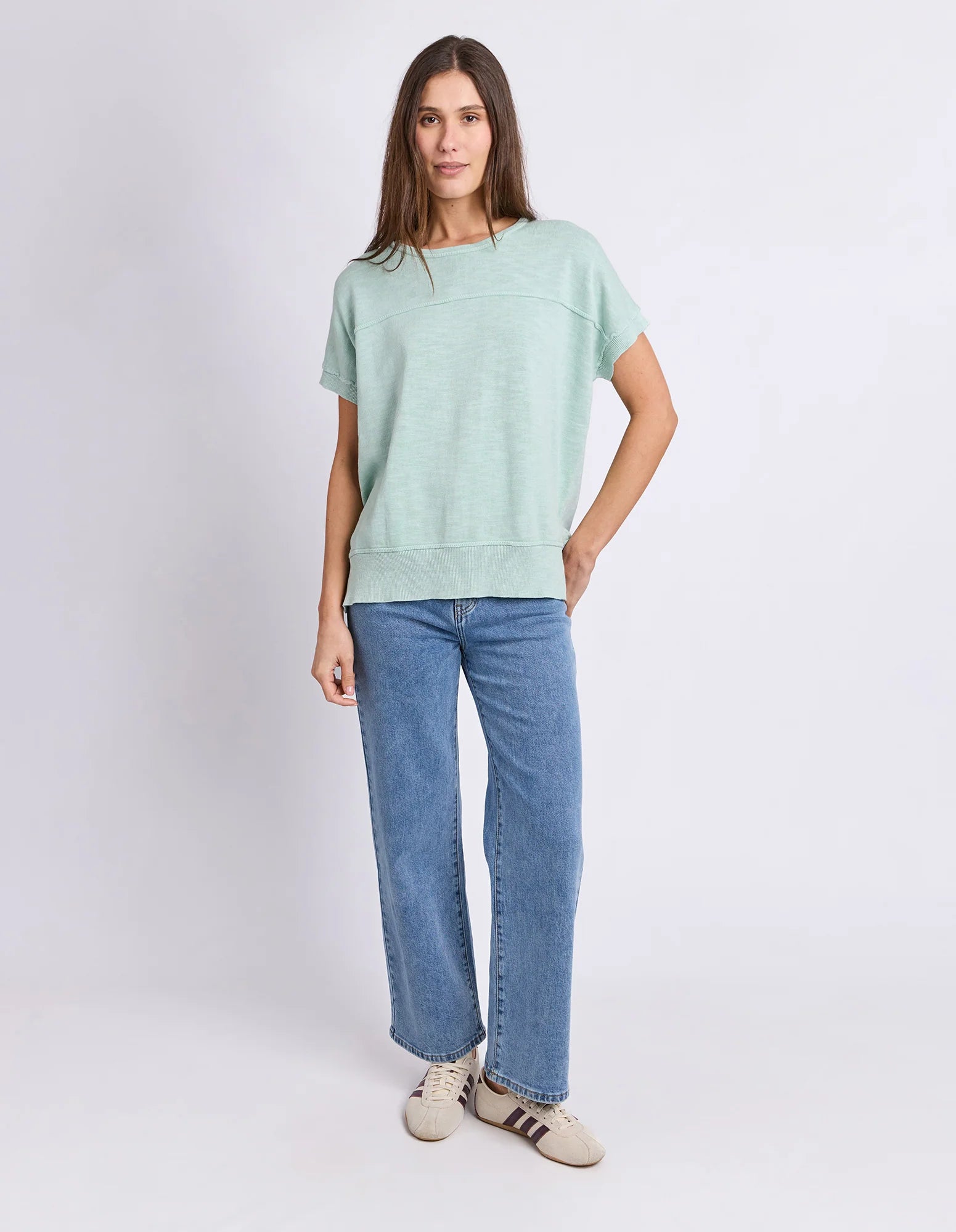 Image of A woman modeling a Foxwood light mint green short-sleeve crewneck sweatshirt, paired with wide-leg blue jeans and beige sneakers, against a plain light gray studio background.