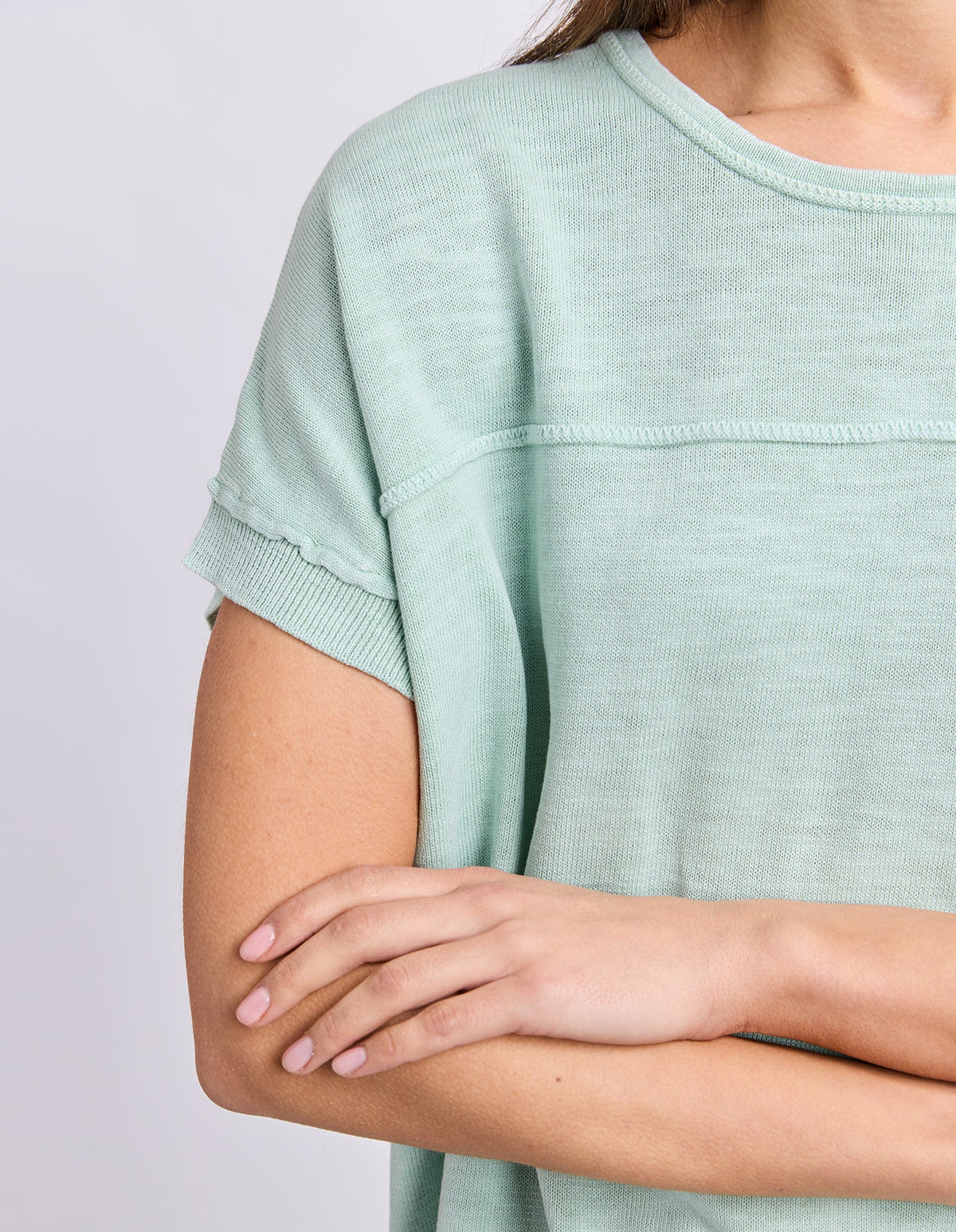 A close-up of a woman wearing a Foxwood pale mint green short-sleeve knit top, showing the ribbed collar, sleeve cuffs, and textured fabric against a light gray background.