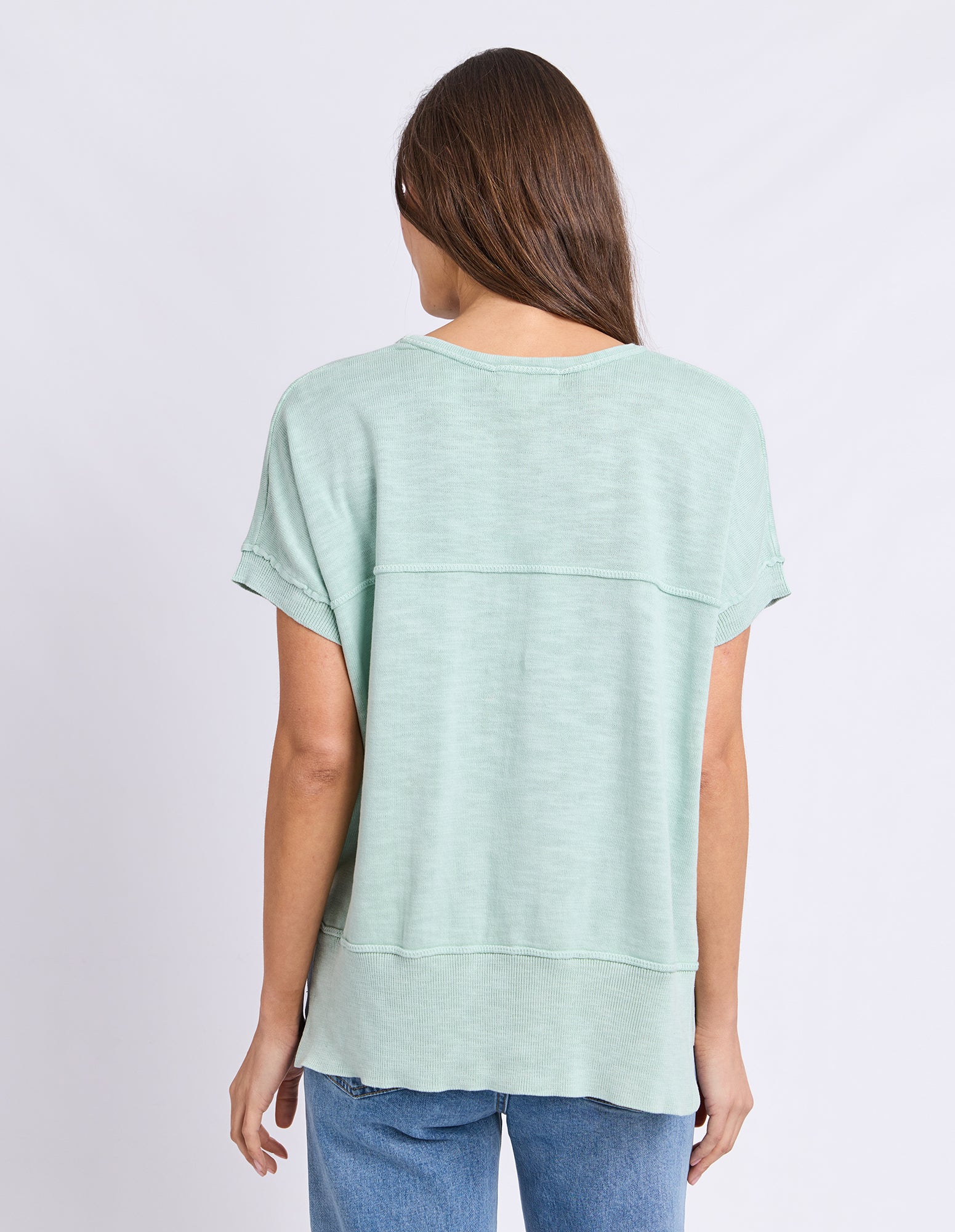 Image of A woman viewed from the back wearing a Foxwood light mint green short-sleeve top and blue jeans against a plain light gray studio background.