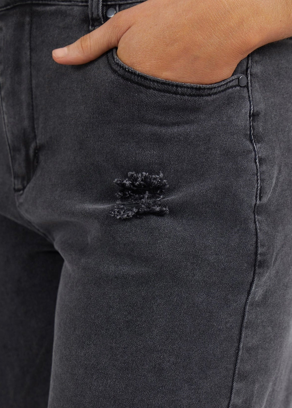 Image of Close-up of Foxwood dark gray washed denim jeans with a hand in the pocket and a small distressed detail near the front.