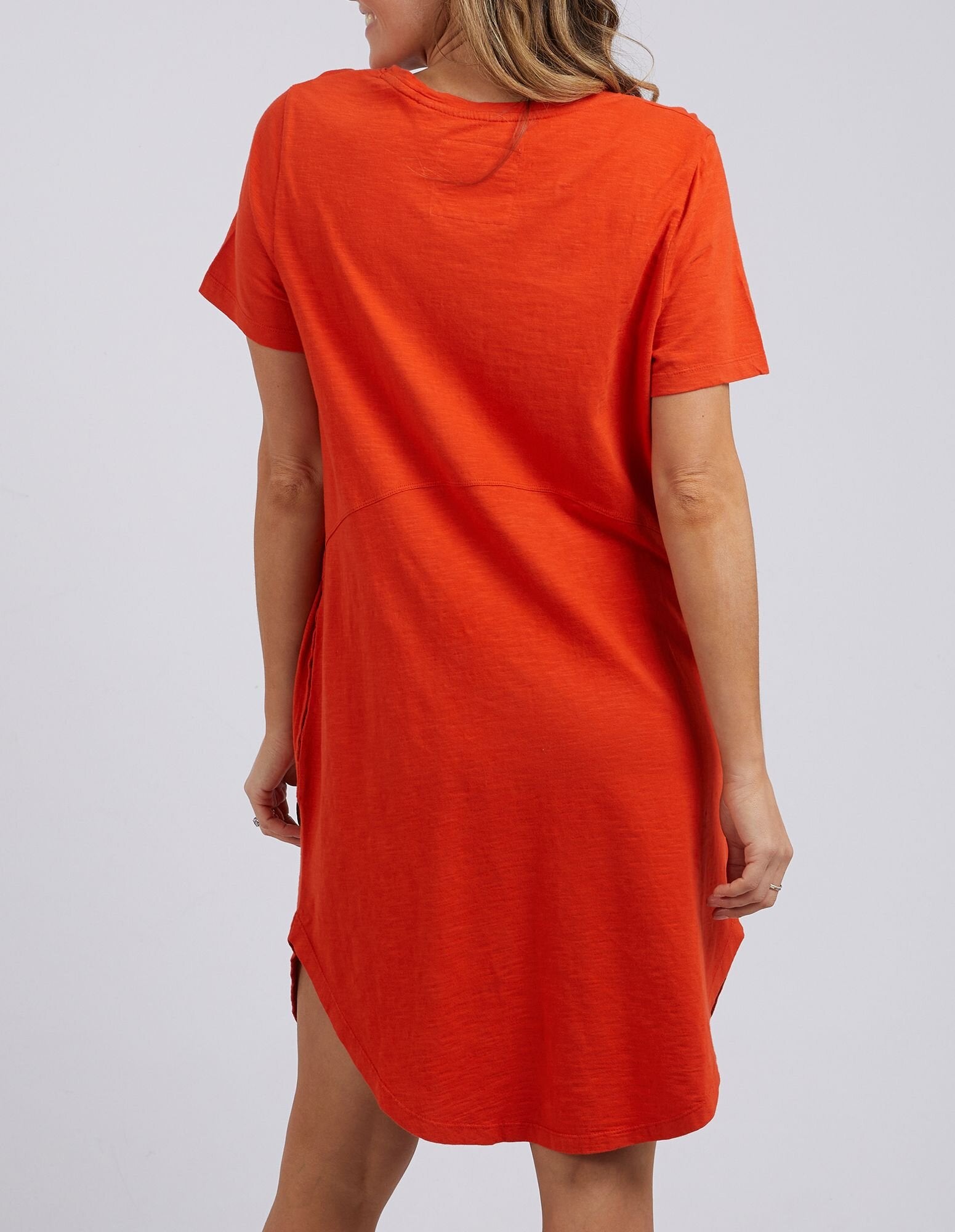 Image of A woman wearing a Foxwood bright orange short-sleeve tunic dress, shown from the back against a light gray studio background.