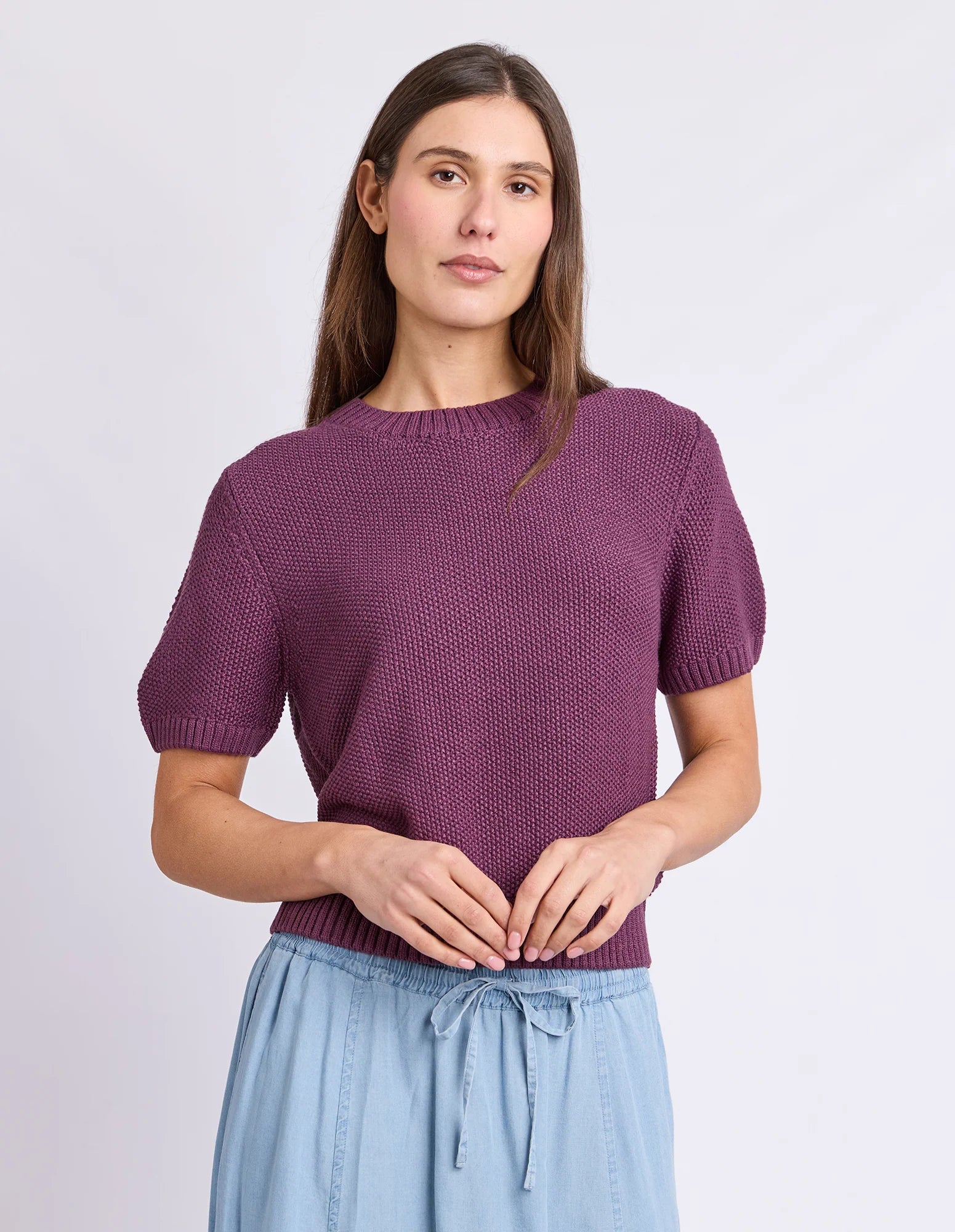 Image of A woman wearing a Foxwood short-sleeve textured knit top in a muted plum purple, paired with light blue drawstring pants, against a plain light gray studio background.