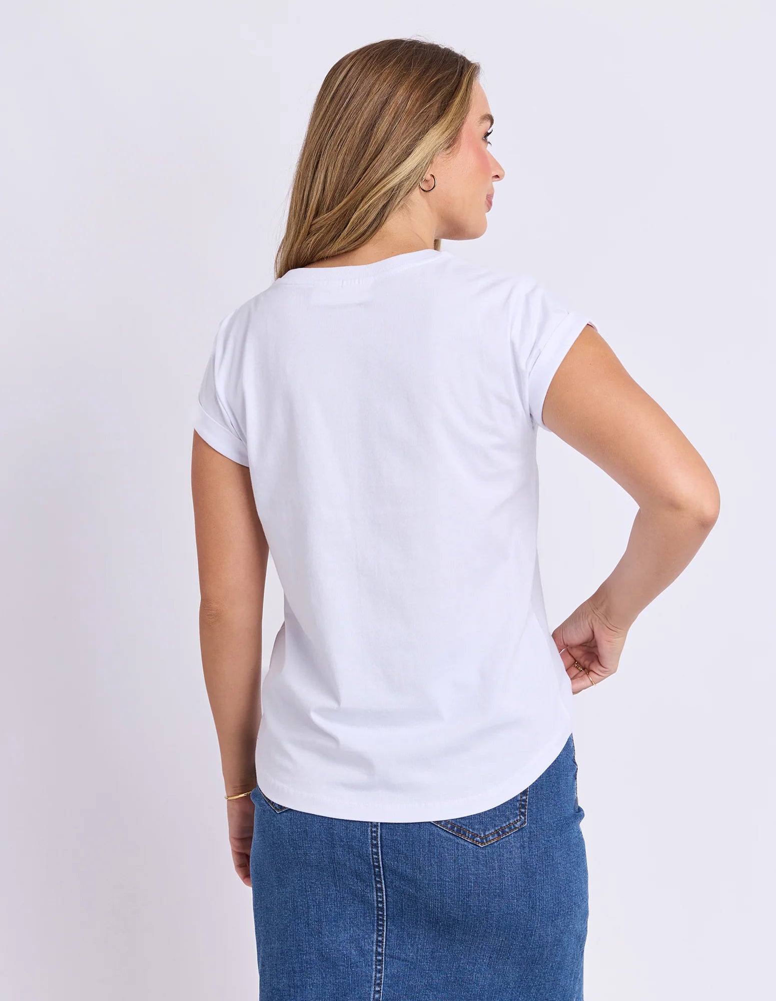 Image of Woman wearing a Foxwood white t-shirt and blue jeans on a light gray background
