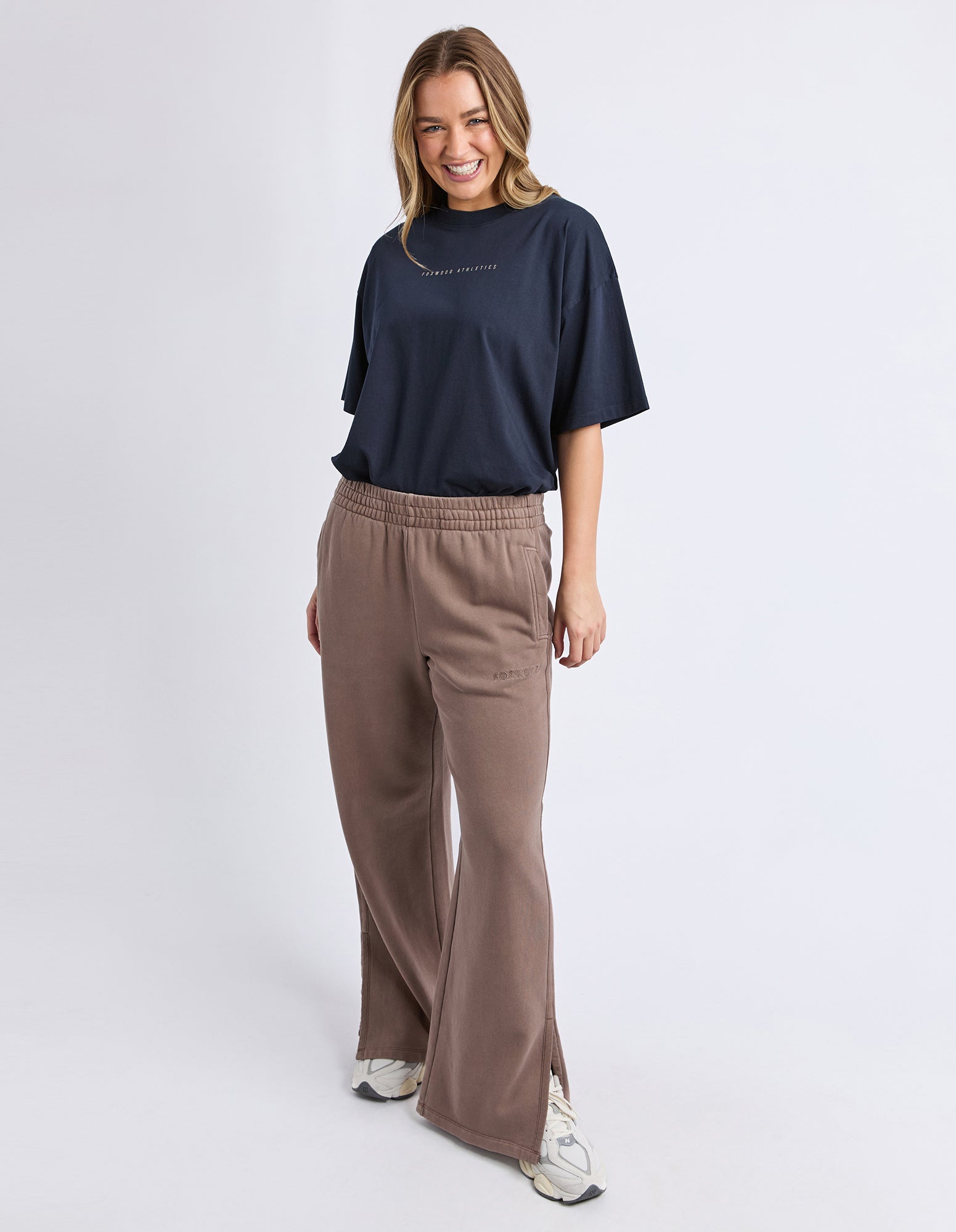 Woman wearing a black t-shirt and Foxwood brown pants on a white background