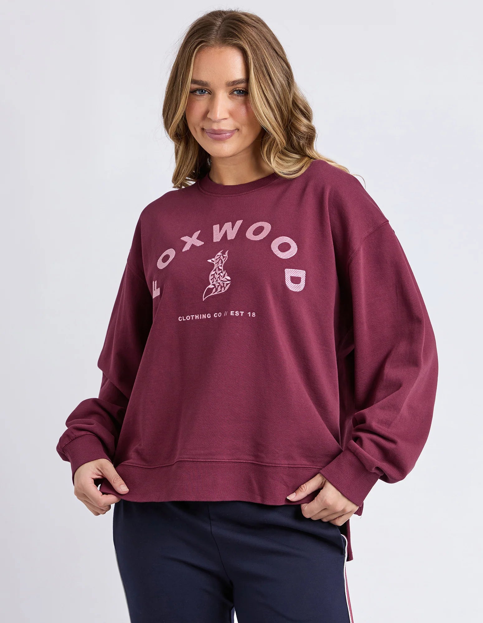 Woman wearing a Foxwood maroon sweatshirt with 'FOXWOOD' branding on a light gray background
