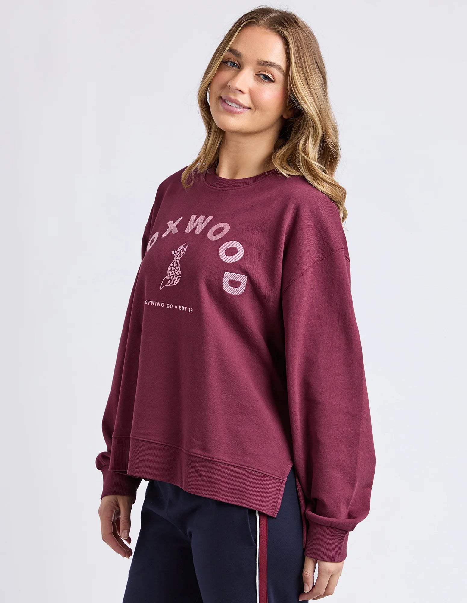 Image of Woman wearing a Foxwood maroon sweatshirt with 'Foxwood' branding on a white background