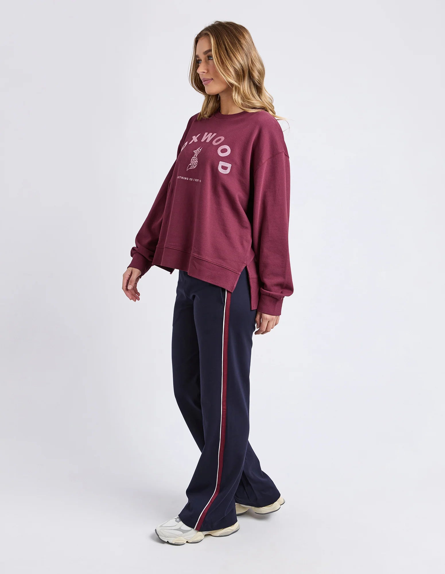 Woman wearing a Foxwood maroon sweatshirt and navy tracksuit with red stripes on a white background