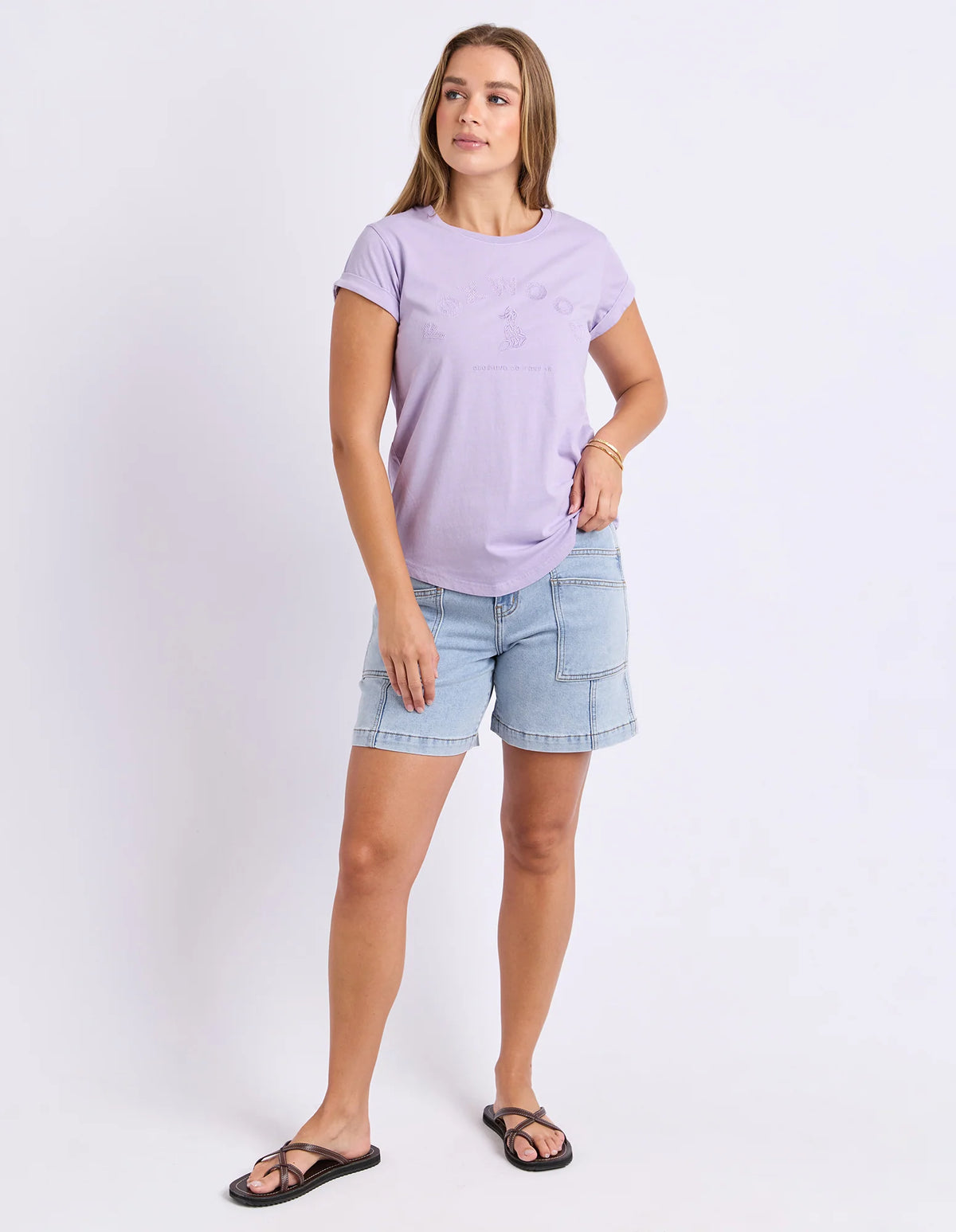 A woman modeling a Foxwood light purple short-sleeve t-shirt and light blue denim shorts against a plain white studio background.