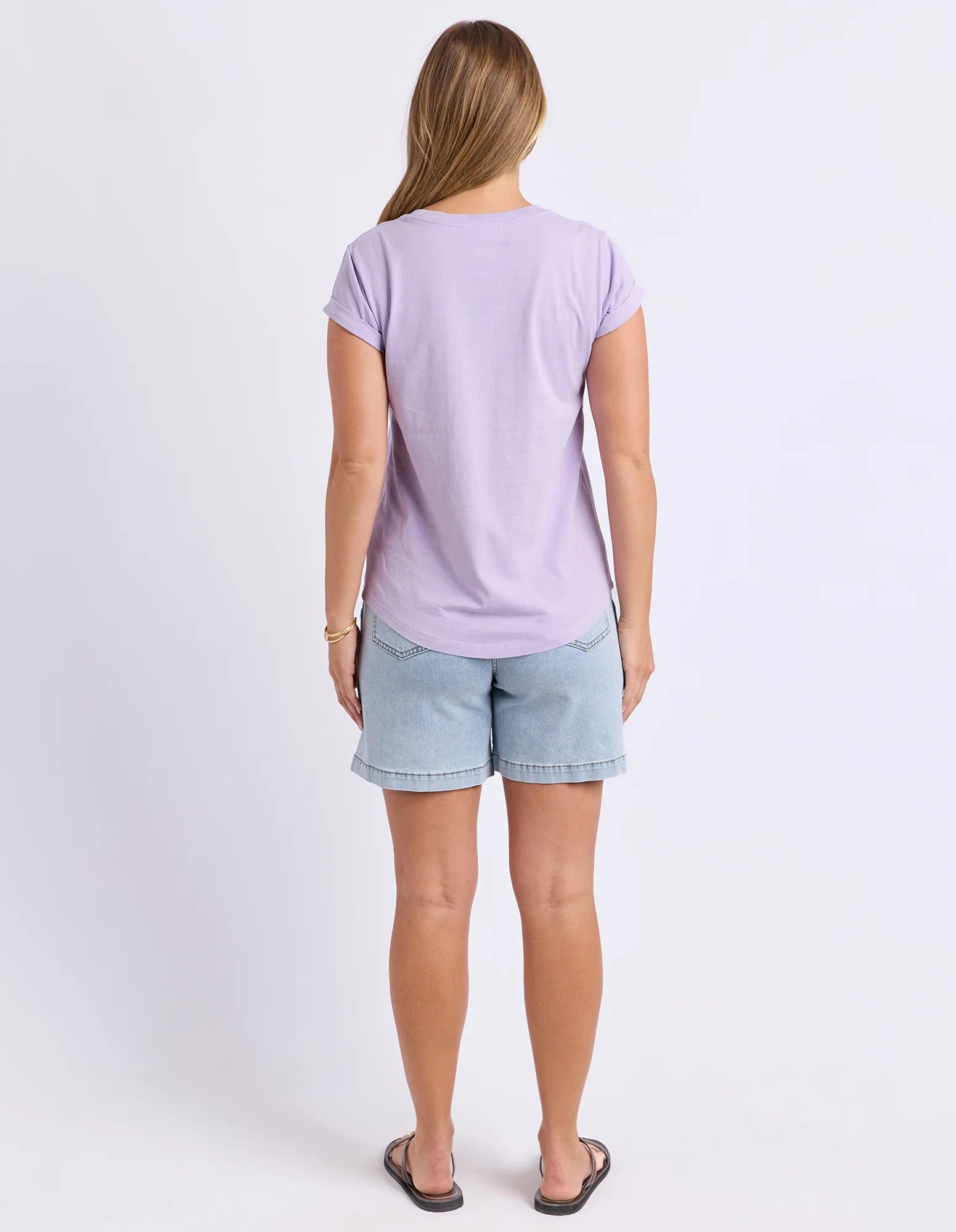 Image of A woman viewed from behind wearing a Foxwood light purple short-sleeve t-shirt and light blue denim shorts against a plain white studio background.