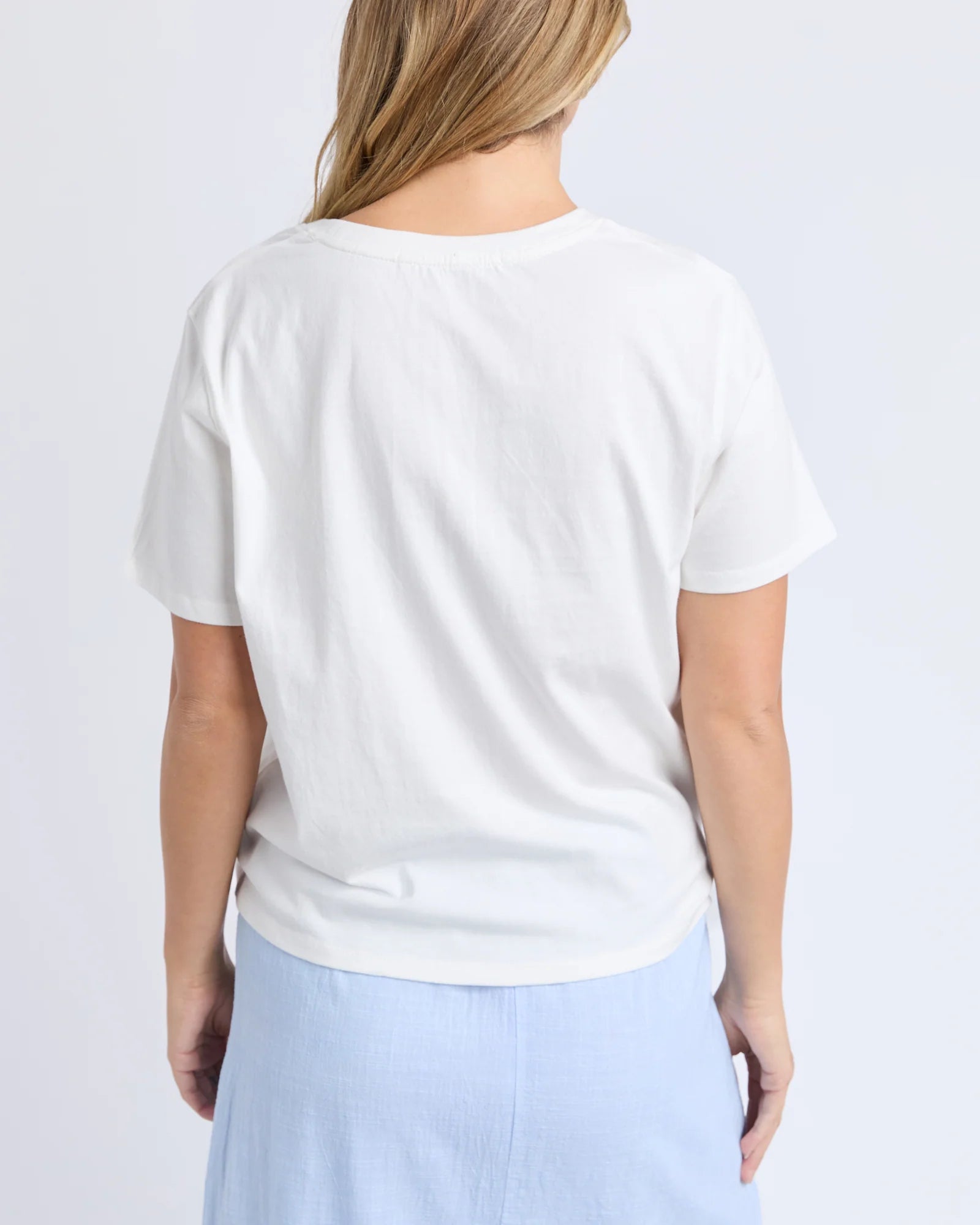 A woman shown from the back wearing a Foxwood plain white short-sleeve crewneck t-shirt and light blue bottoms, against a light gray studio background.