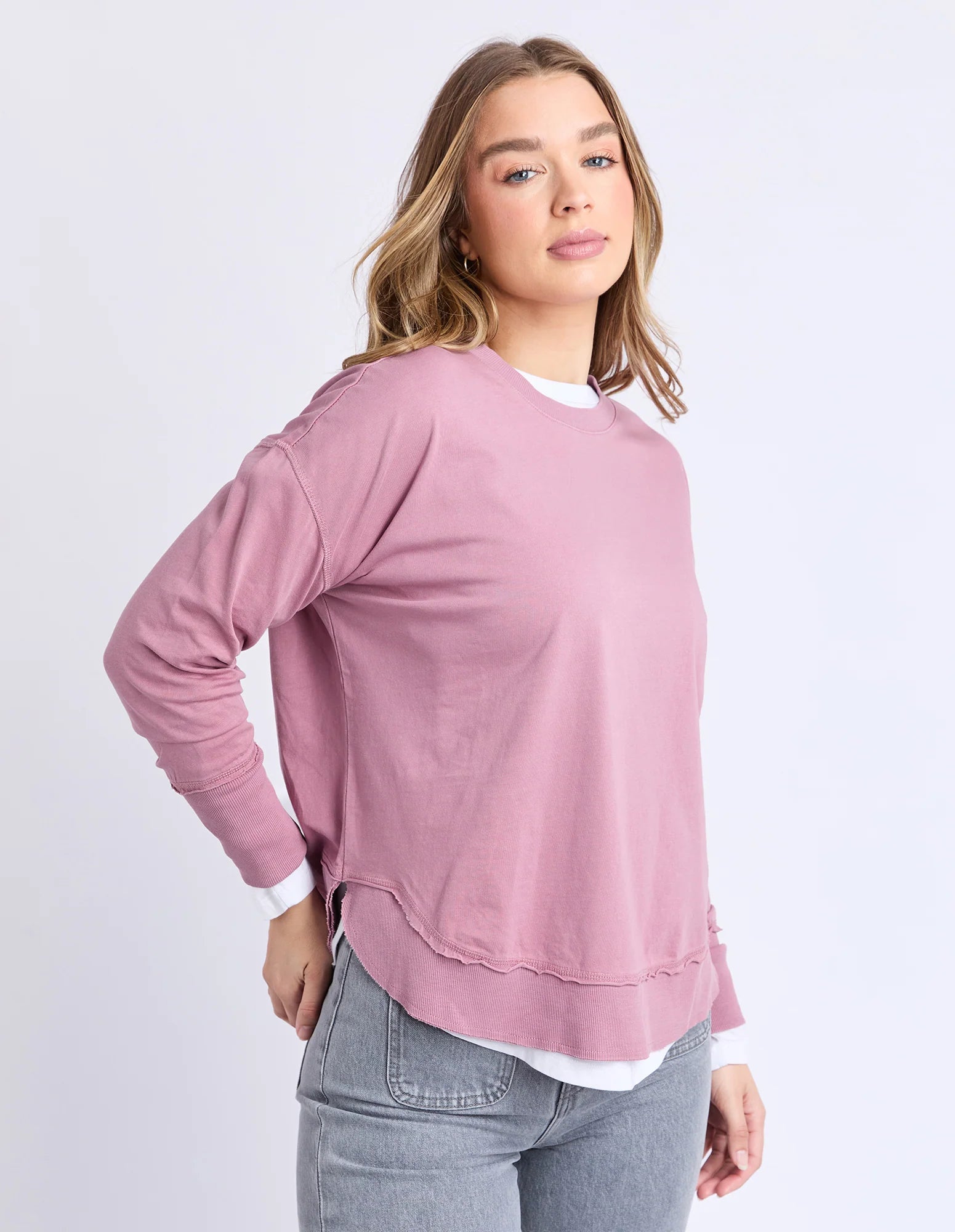 Image of Woman wearing a Foxwood pink sweater and gray jeans on a white background