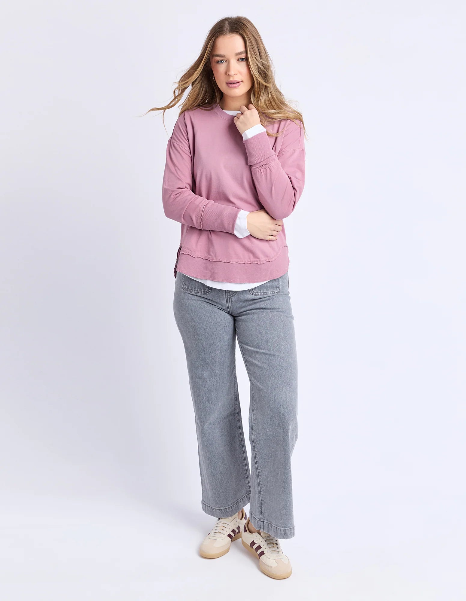 Image of Woman wearing a Foxwood pink sweater and gray pants on a white background