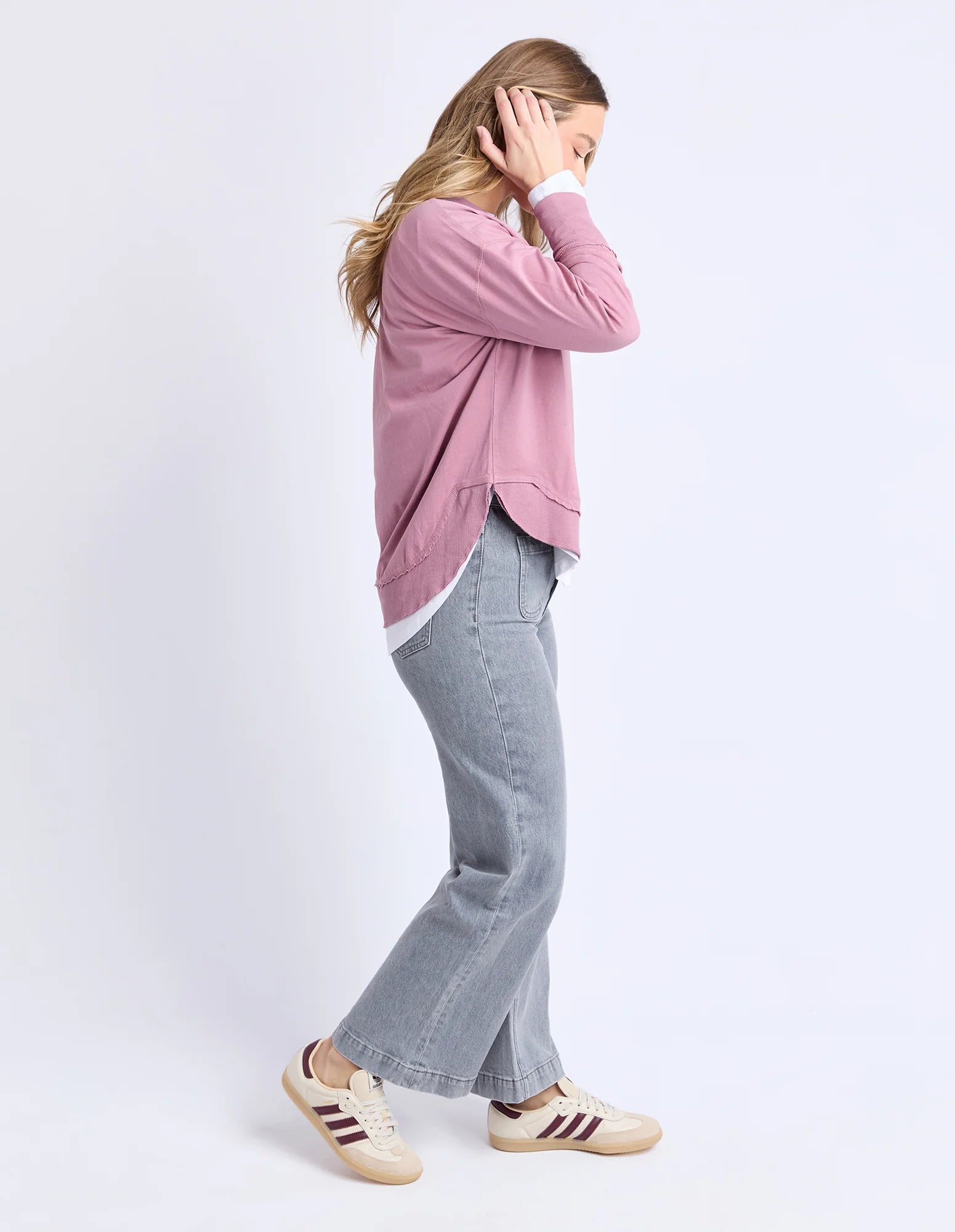 Image of Woman wearing a Foxwood pink sweater and gray jeans on a white background