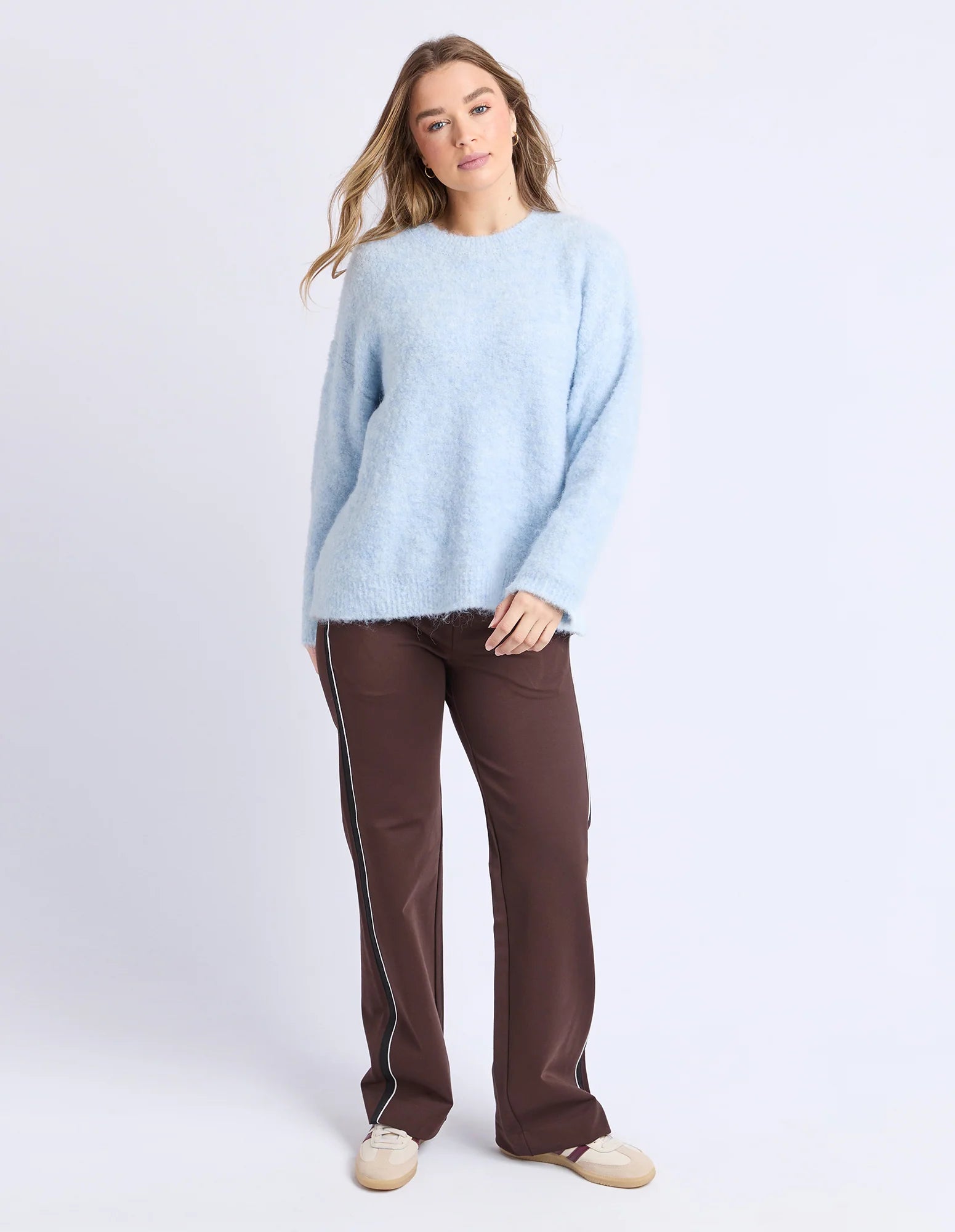 Woman wearing a Foxwood light blue sweater and brown pants on a white background