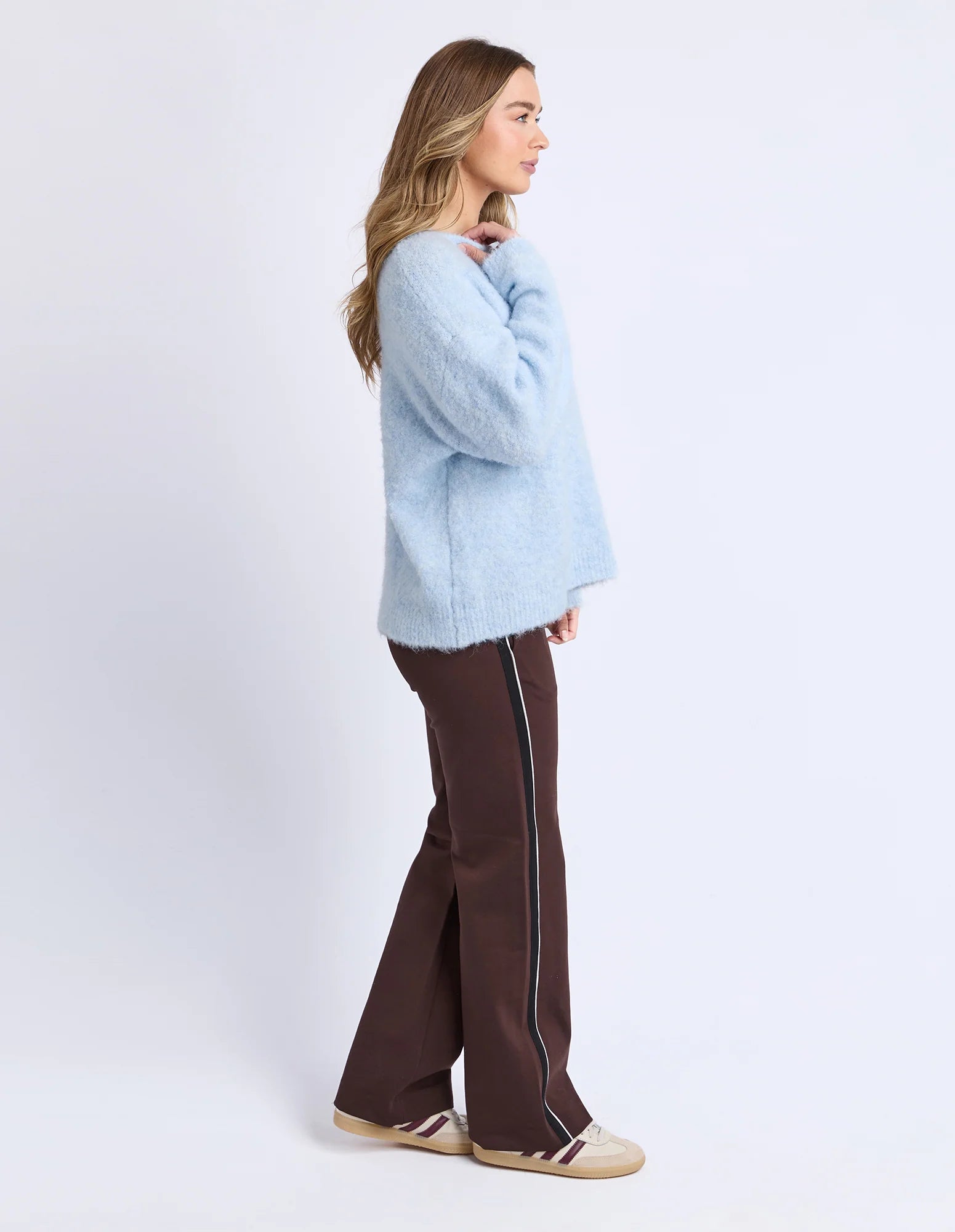 Image of Woman wearing a Foxwood light blue sweater and brown pants with white stripes on a white background