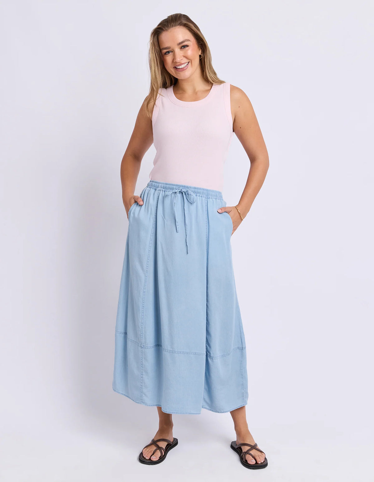 Woman wearing a Foxwood light pink sleeveless top and light blue skirt on a white background