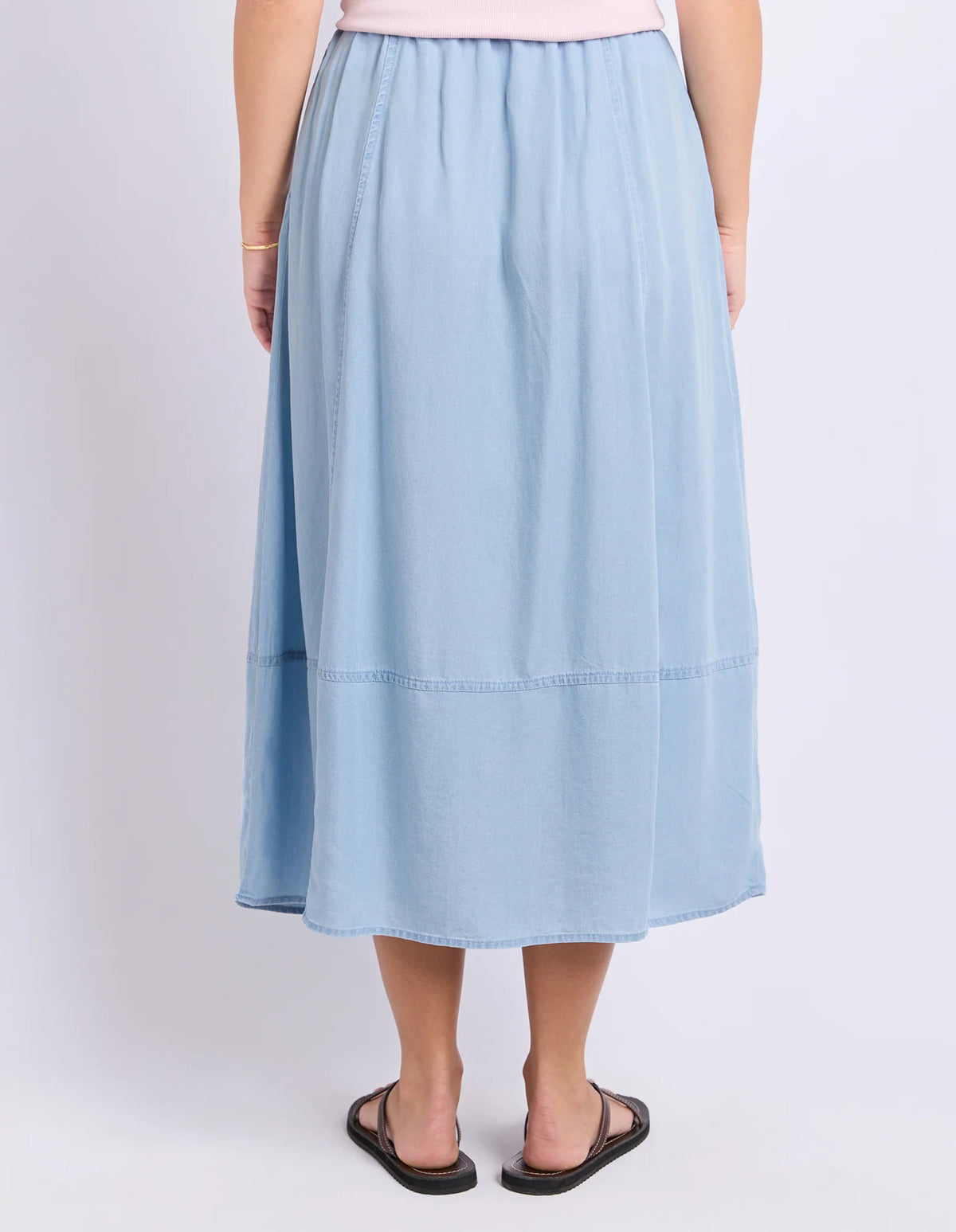 A woman shown from the back wearing a Foxwood light blue midi skirt with a gathered waist and a straight, flowing silhouette, paired with black sandals against a plain light gray studio background.