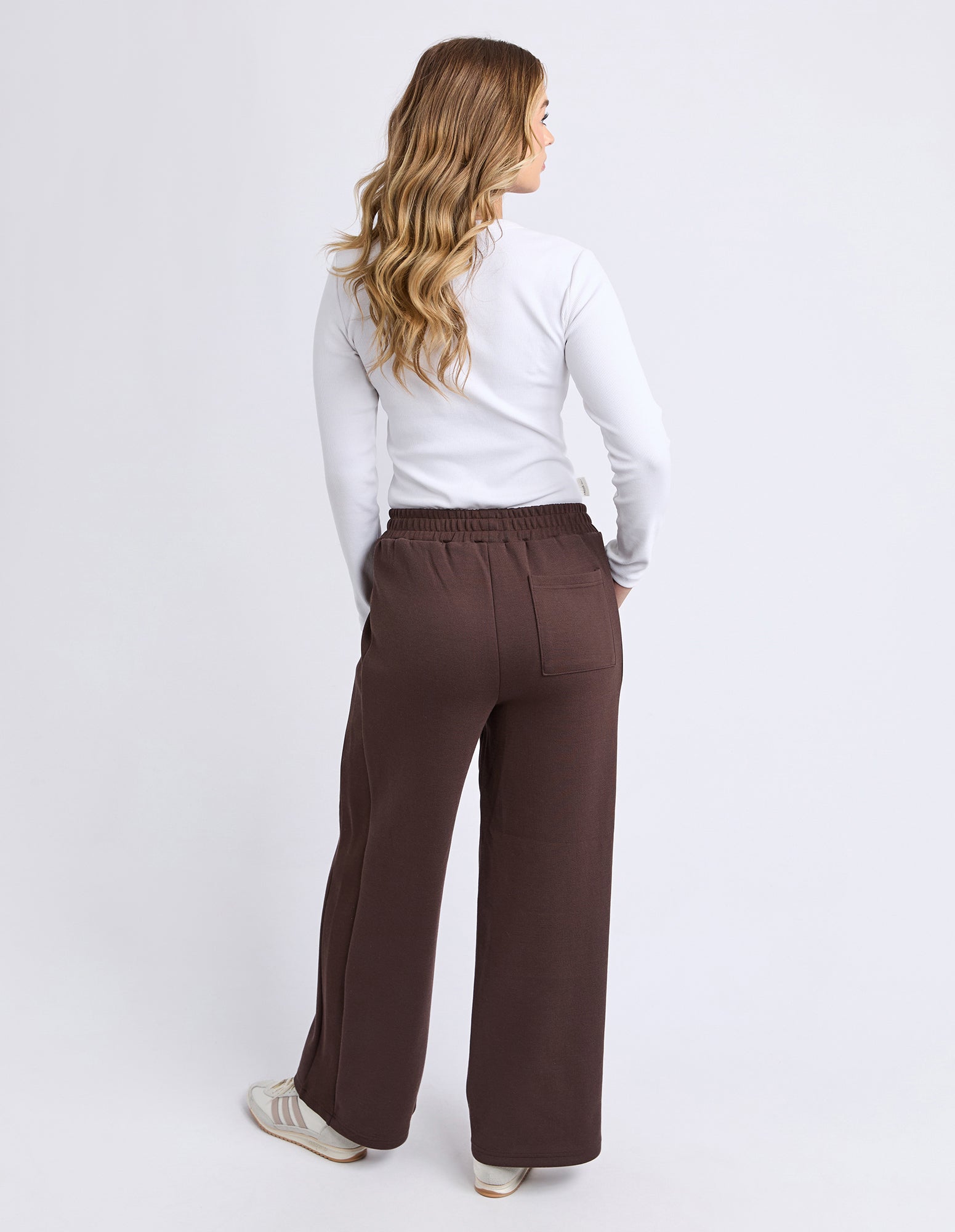 Image of Woman wearing Foxwood brown pants and a white top on a light gray background