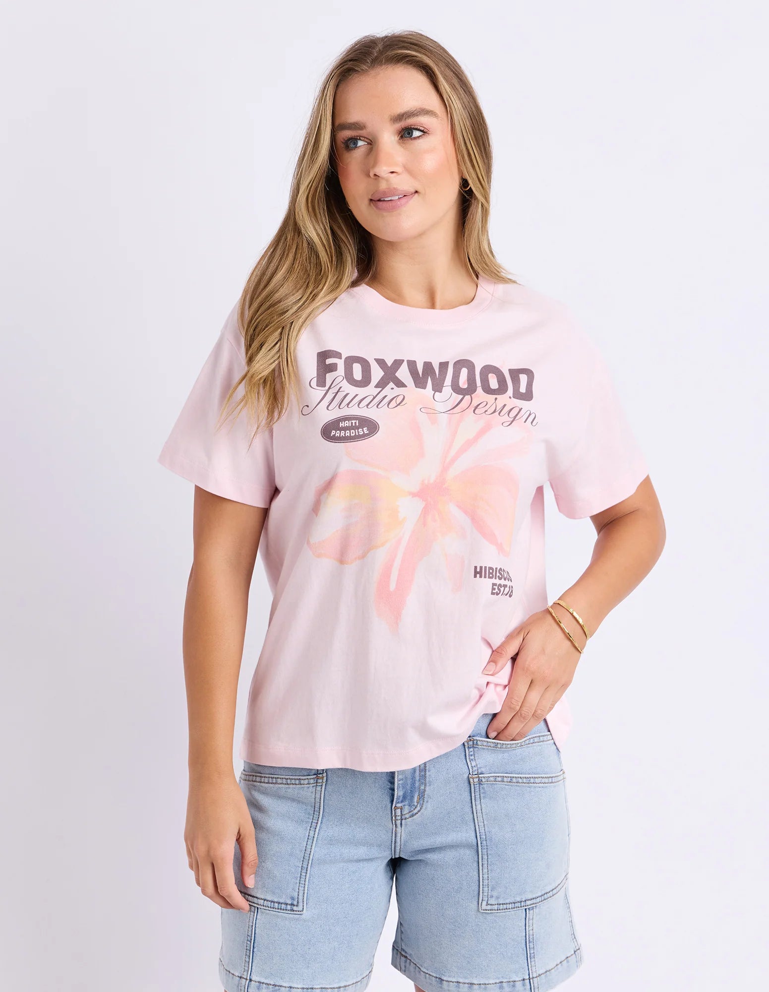 Image of Woman wearing Foxwood printed hisbiscus shirt paired with denim jeans on a plain background 