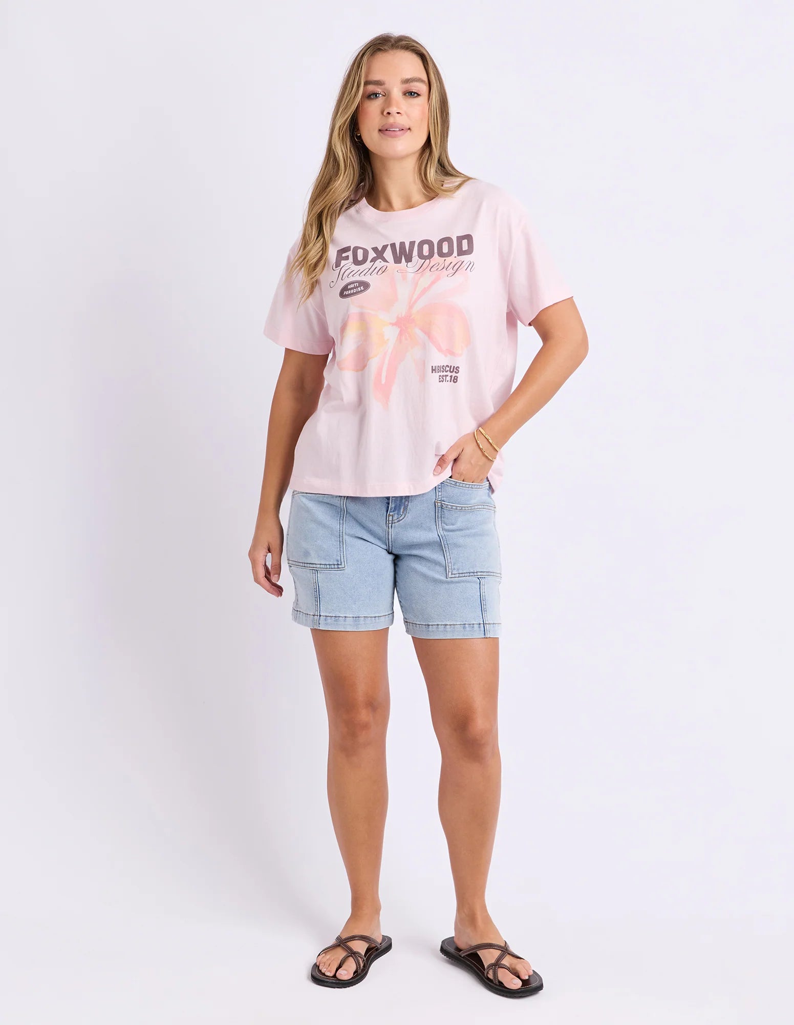 Image of Woman wearing Foxwood printed hisbiscus shirt paired with denim jeans on a plain background 