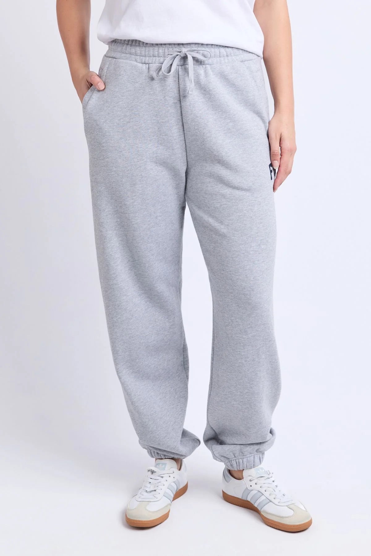 Image of Woman wearing grey Foxwood trackpants with a white top on a plain background 