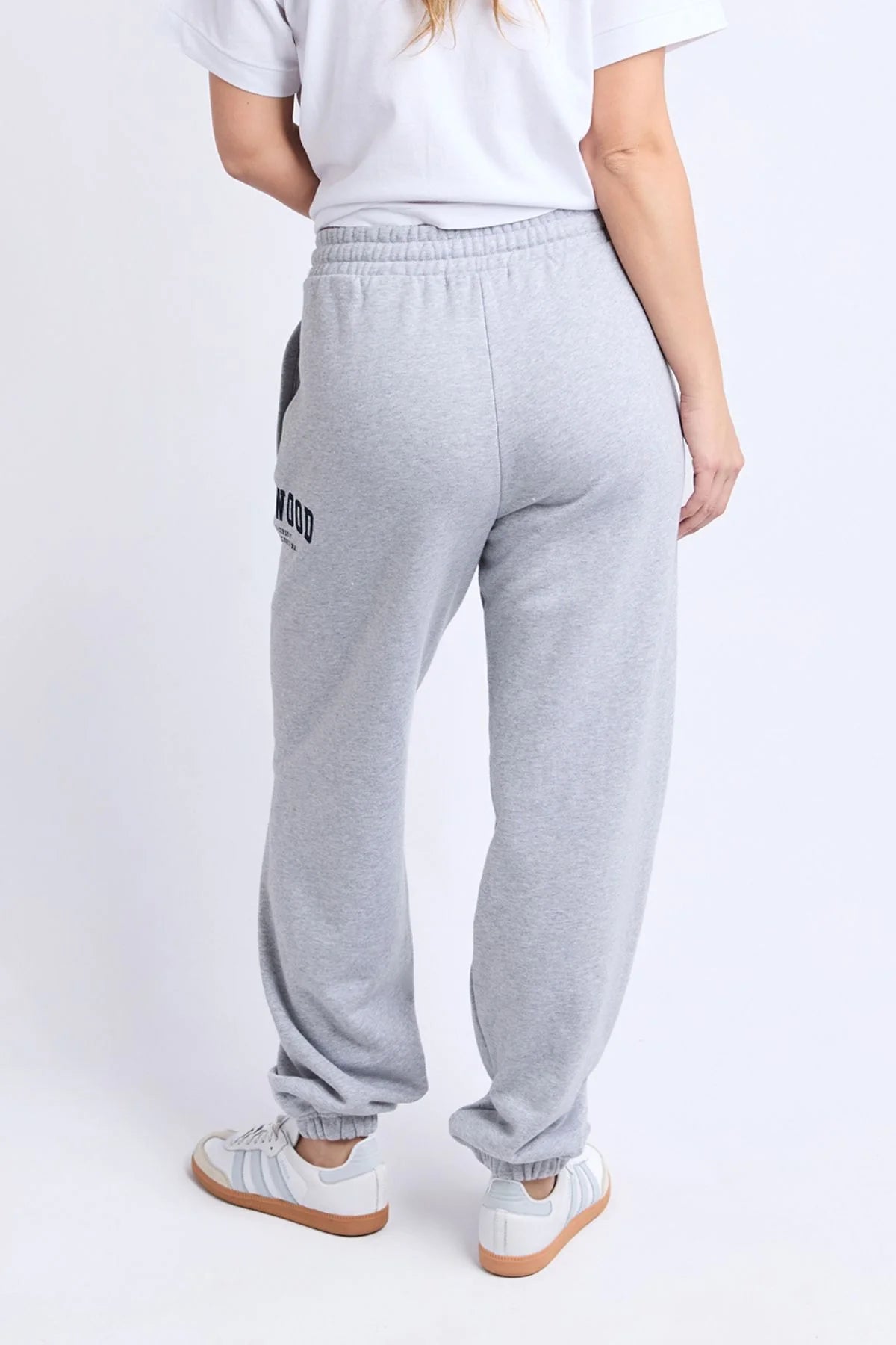 Woman wearing grey Foxwood trackpants with a white top on a plain background 
