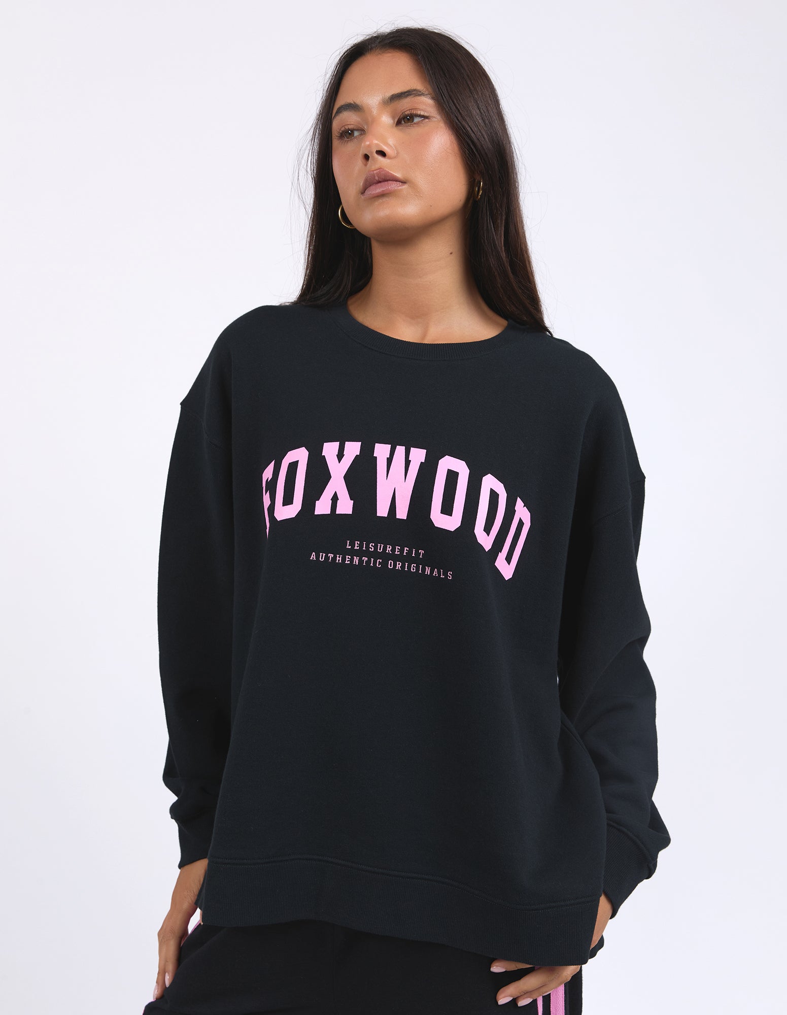 Image of A female model wearing a black sweatshirt with 'FOXWOOD INTERVAL' text in neon pink on the front chest and a large pink print on the back and sleeves.