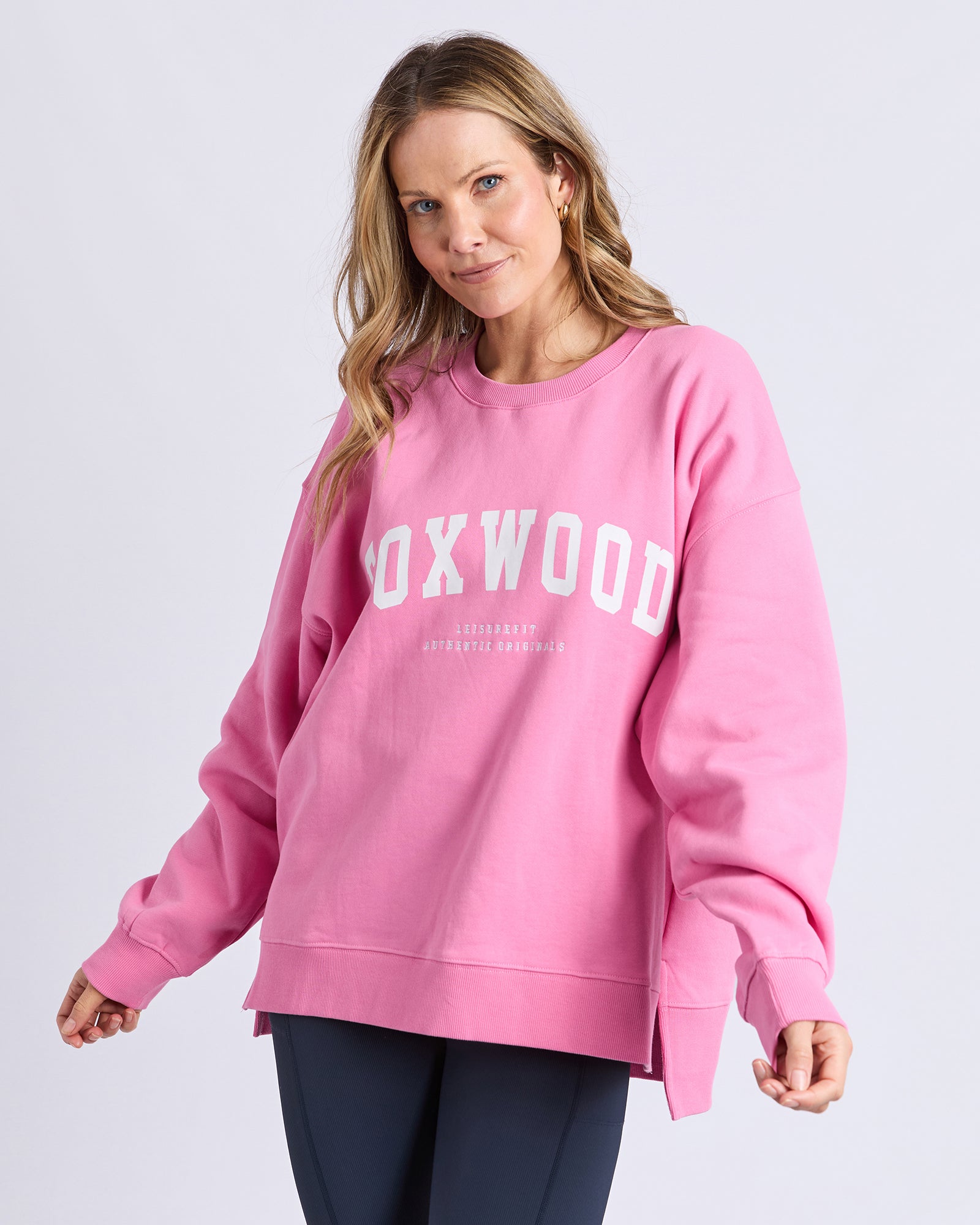 Image of Woman wearing a pink sweatshirt with 'FOXWOOD' printed on it against a light gray background
